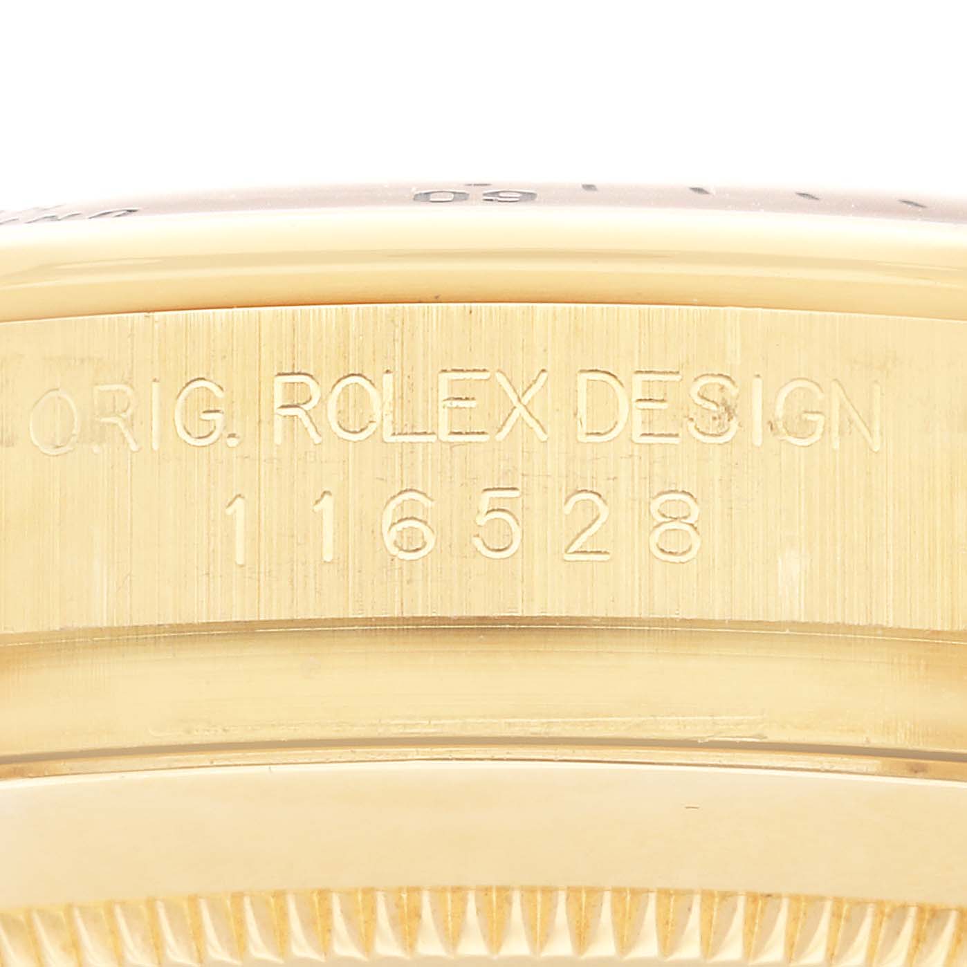 This image shows a close-up of the edge of a Rolex Daytona 116528 Men's Yellow Gold Mother of Pearl Dial 116528 Men's Yellow Gold Mother of Pearl Dial watch, featuring the model number 116528 and "ORIG. ROLEX DESIGN" engraving.