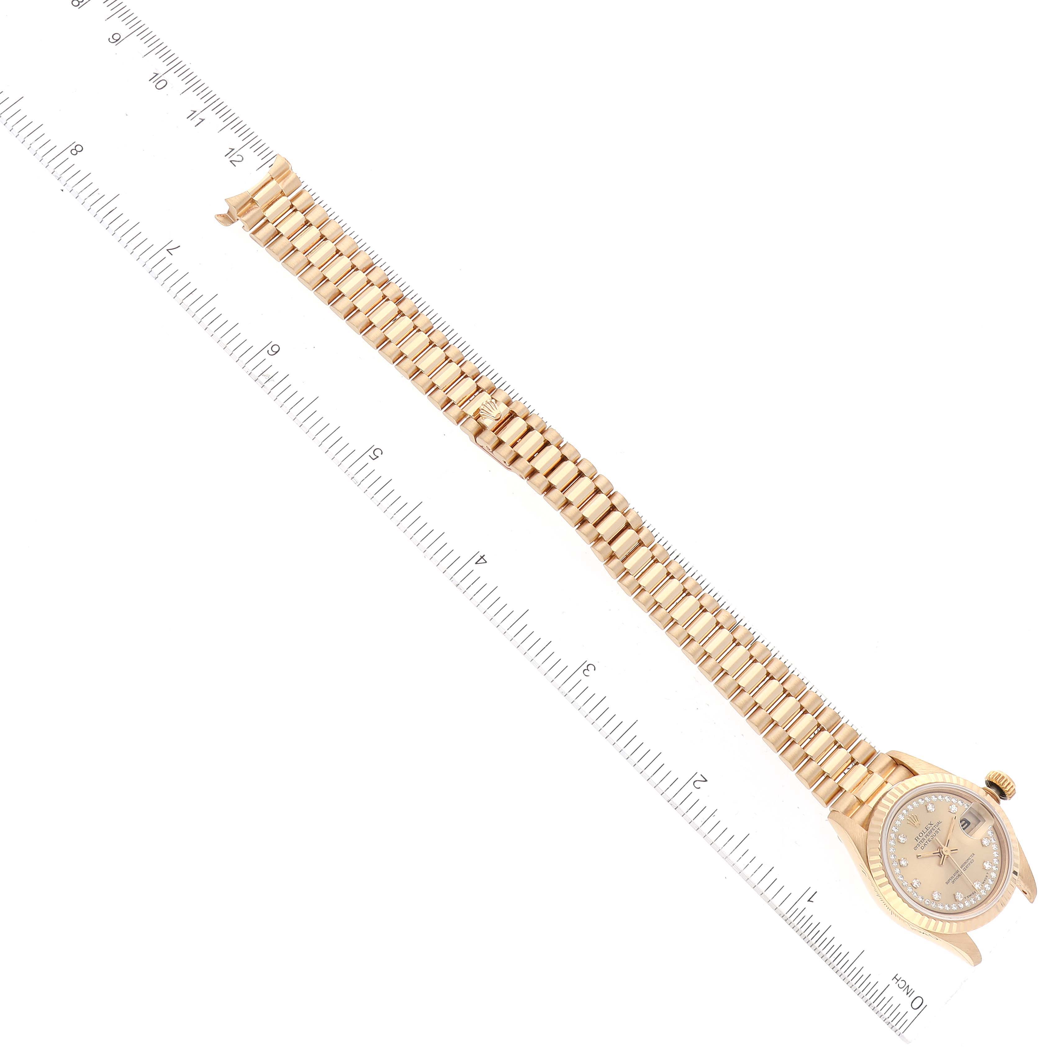 This image shows a Rolex President 69178 Women
s Yellow Gold Champagne Dial 69178 Women
s Yellow Gold Champagne Dial model watch laid flat with the face and band fully visible, positioned next to a ruler.