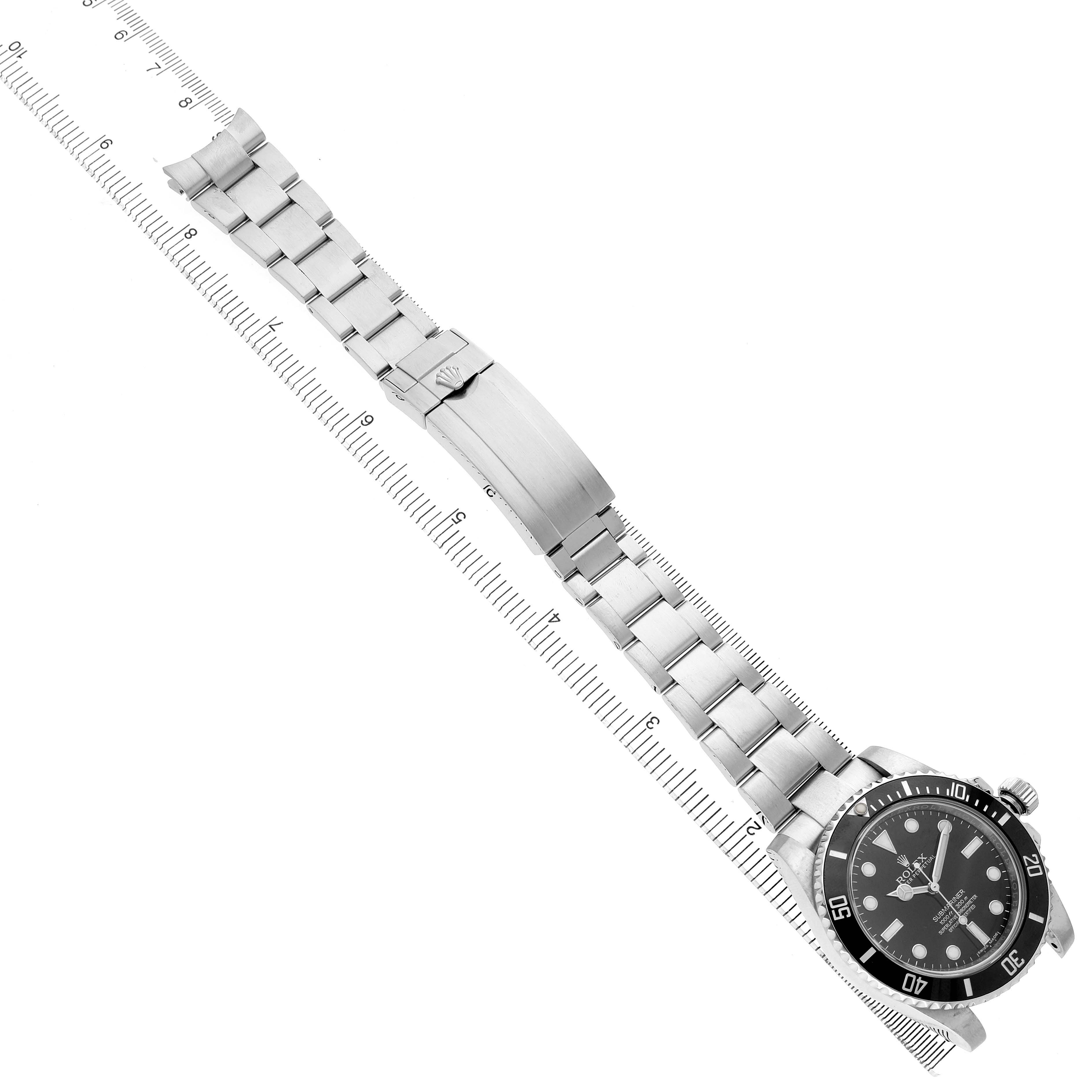The Rolex Submariner 114060 Men's Stainless Steel Black Dial watch is displayed at an angle, showing the face, bezel, and full metal bracelet alongside a ruler for scale.