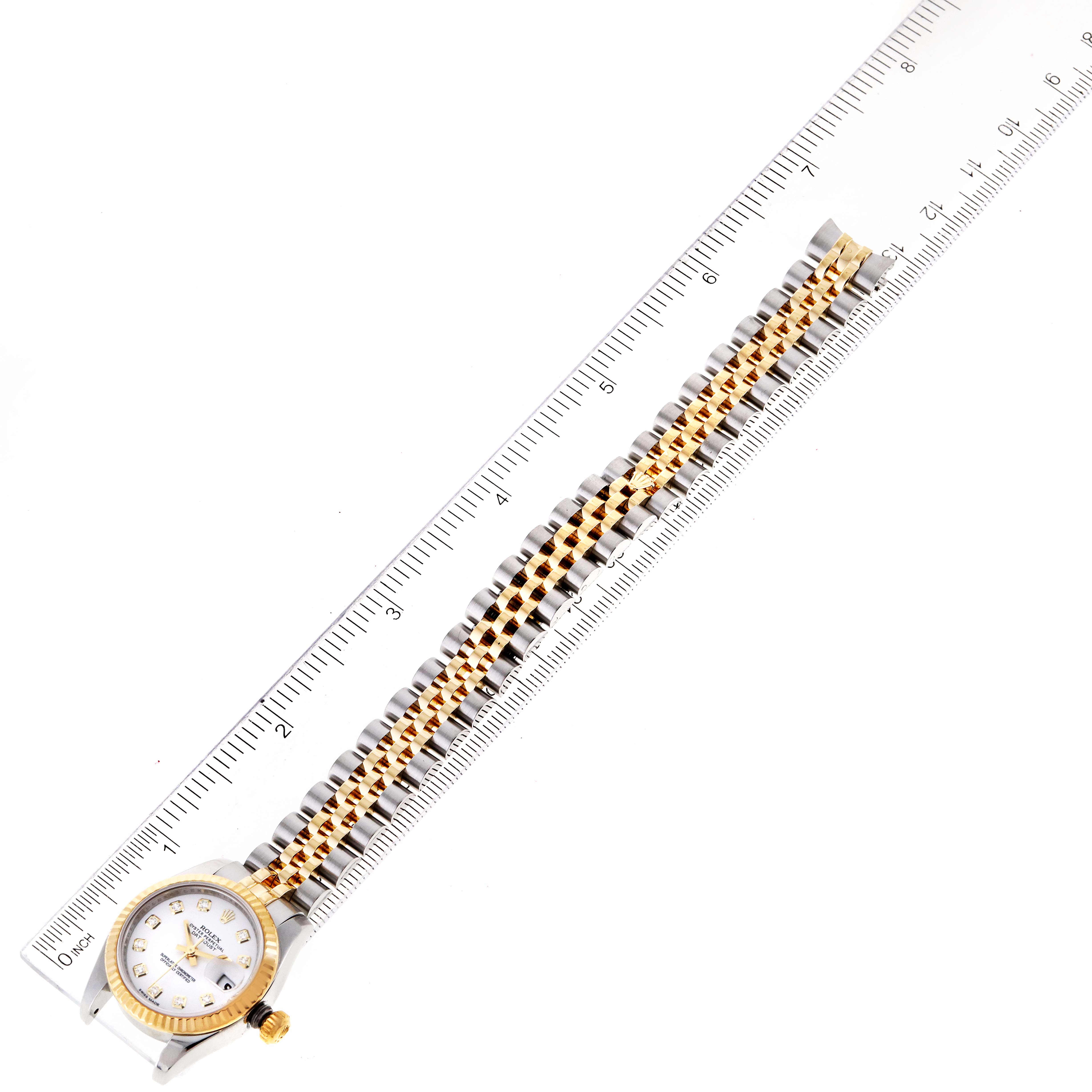 The image shows a top-down view of a Rolex Datejust 179173 Women's Steel and Gold (two tone) White Dial 179173 Women's Steel and Gold (two tone) White Dial watch, highlighting its face, gold bezel, and two-tone bracelet next to a ruler for scale.