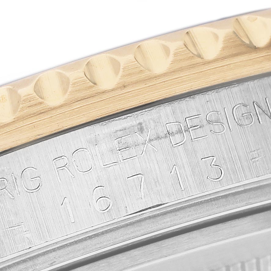 The image shows a close-up of the bezel and engraved case of a Rolex GMT-Master 16713LN Men's Steel and Gold (two tone) Black Dial 16713LN Men's Steel and Gold (two tone) Black Dial.