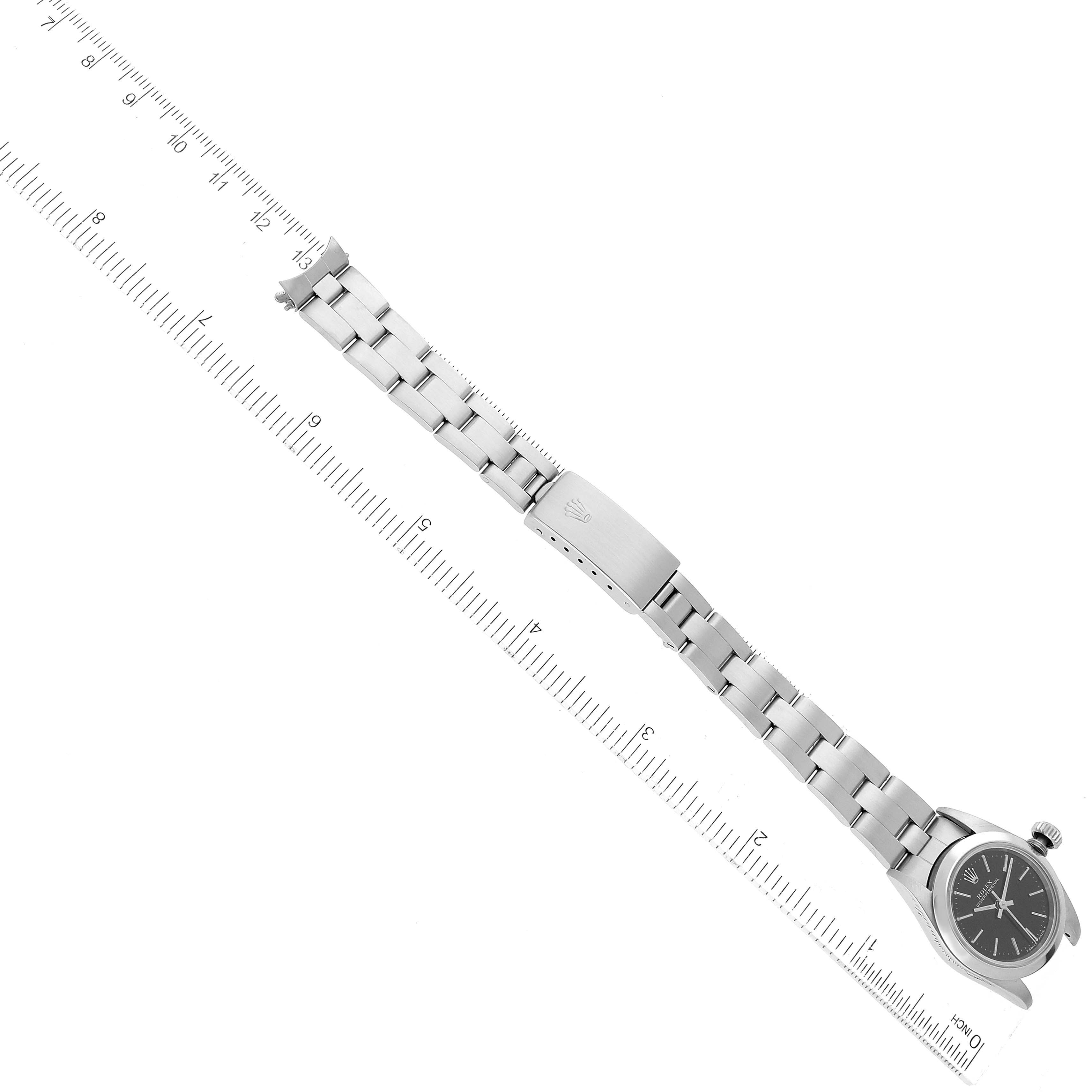 The image shows a Rolex Oyster Perpetual 67180 Women's Stainless Steel Black Dial 67180 Women's Stainless Steel Black Dial watch laid flat, displaying its face, bracelet, and clasp, with a ruler for scale.