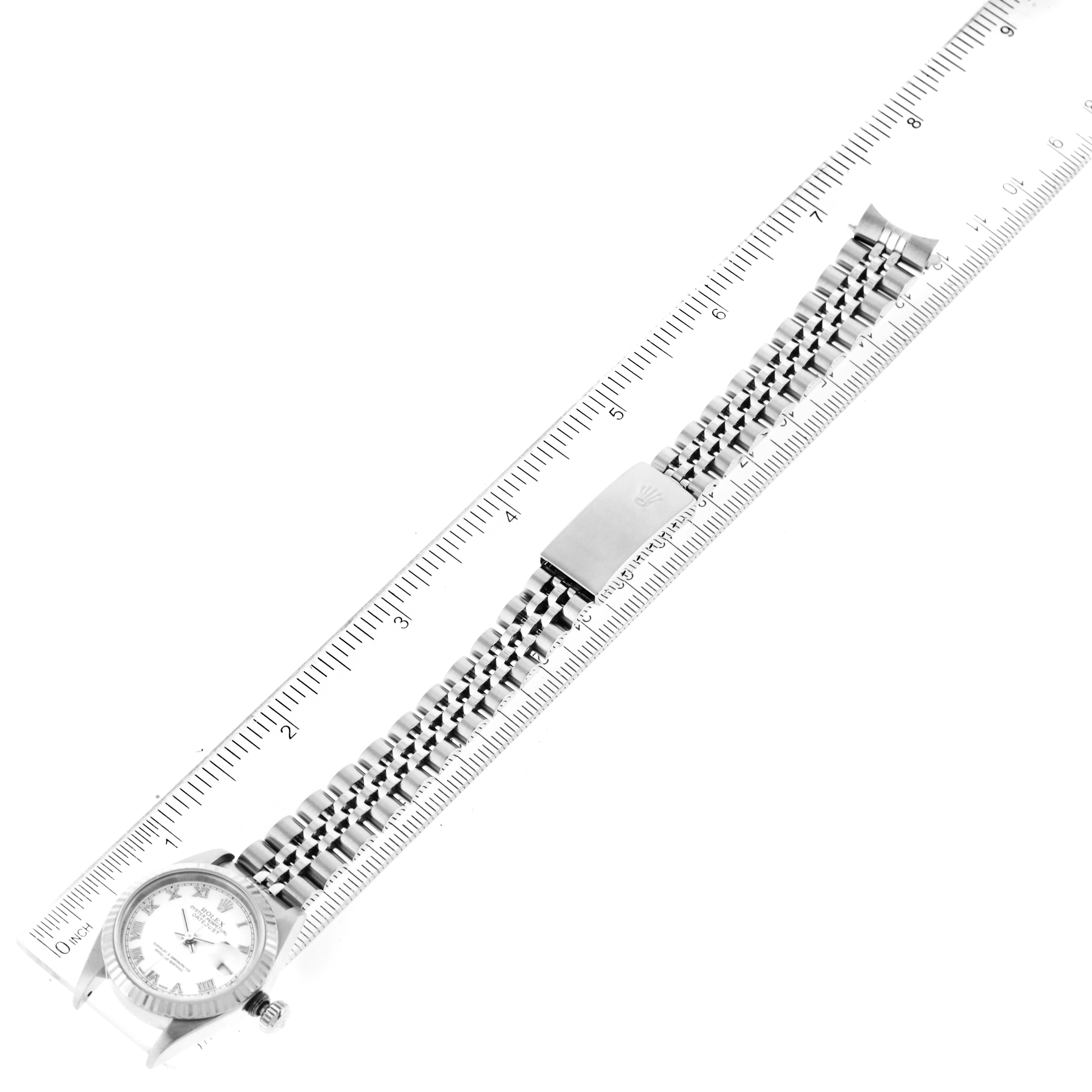 The Rolex Datejust 79174 Women's Stainless Steel White Dial 79174 Women's Stainless Steel White Dial watch is shown from a top-down angle, including the face, bracelet, and clasp, positioned next to a ruler.