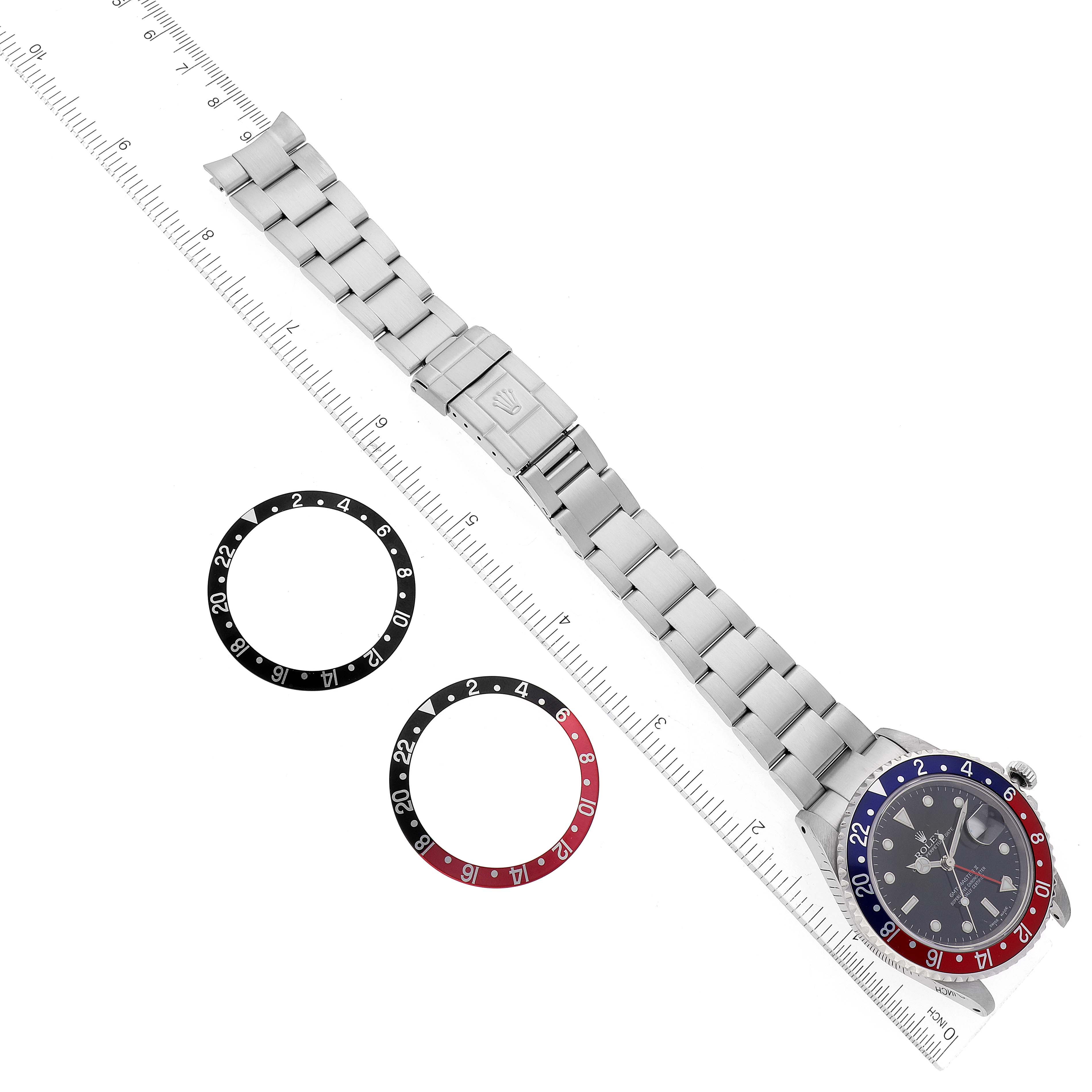 The GMT-Master Rolex watch is shown flat with its bracelet extended, alongside two interchangeable bezels on a ruler for size reference.