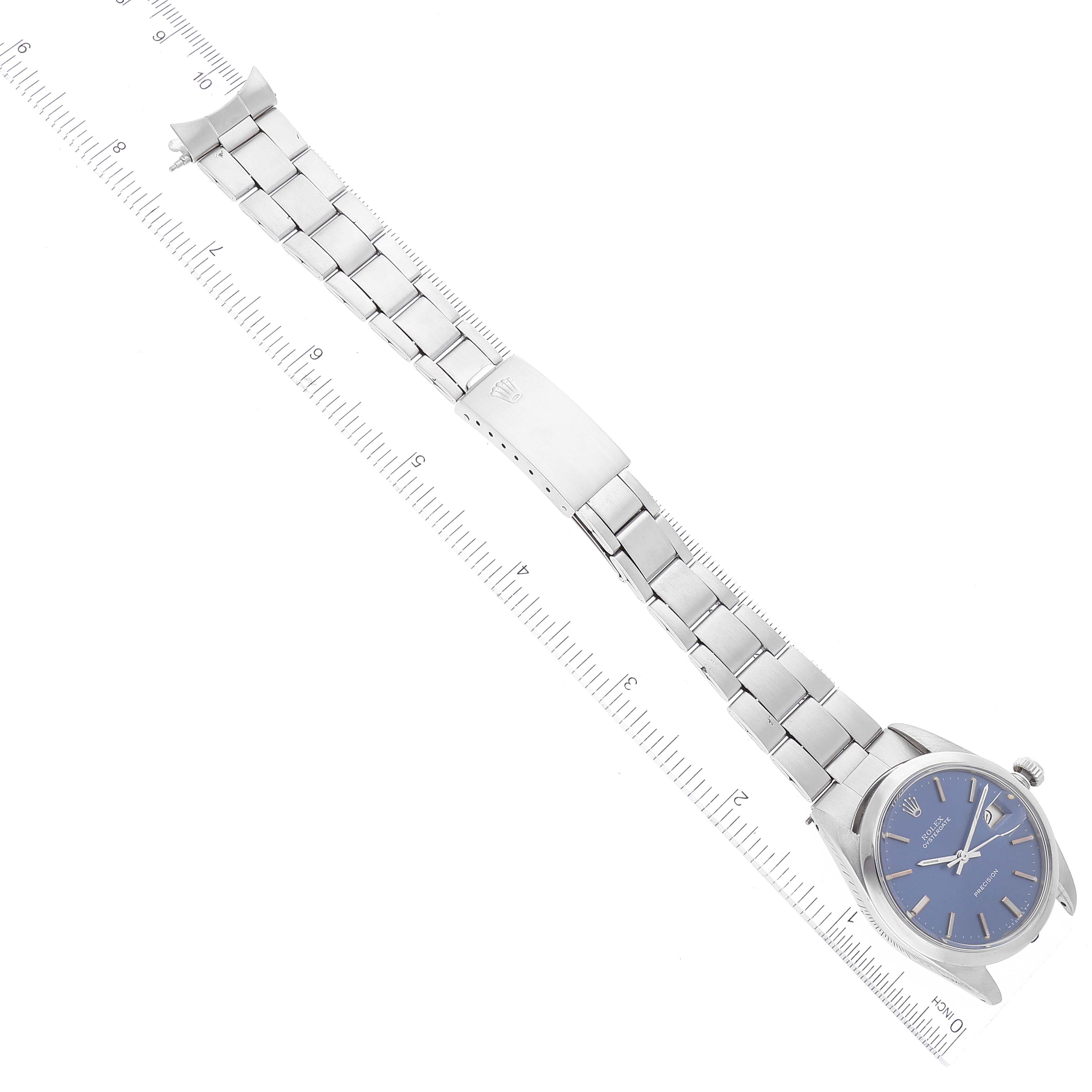 The image shows a Rolex Vintage Collection 6694 Men's Stainless Steel Blue Dial 6694 Men's Stainless Steel Blue Dial watch laid flat with its face and metal bracelet visible, alongside a measuring tool.