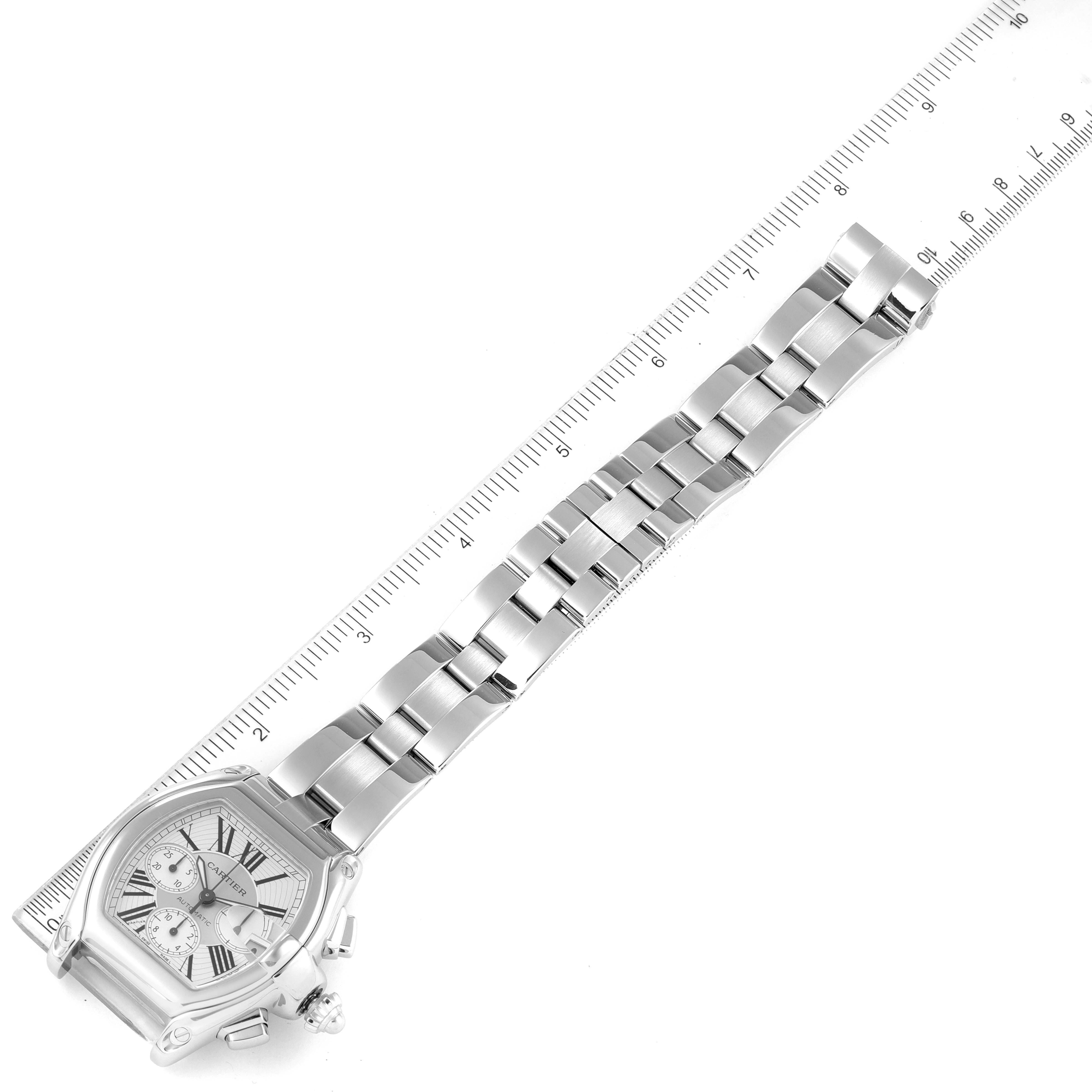 The image shows a top-down view of a Cartier Roadster W62019X6 Men
s Stainless Steel Silver Dial W62019X6 Men
s Stainless Steel Silver Dial watch, highlighting the watch face and metal band next to a ruler.