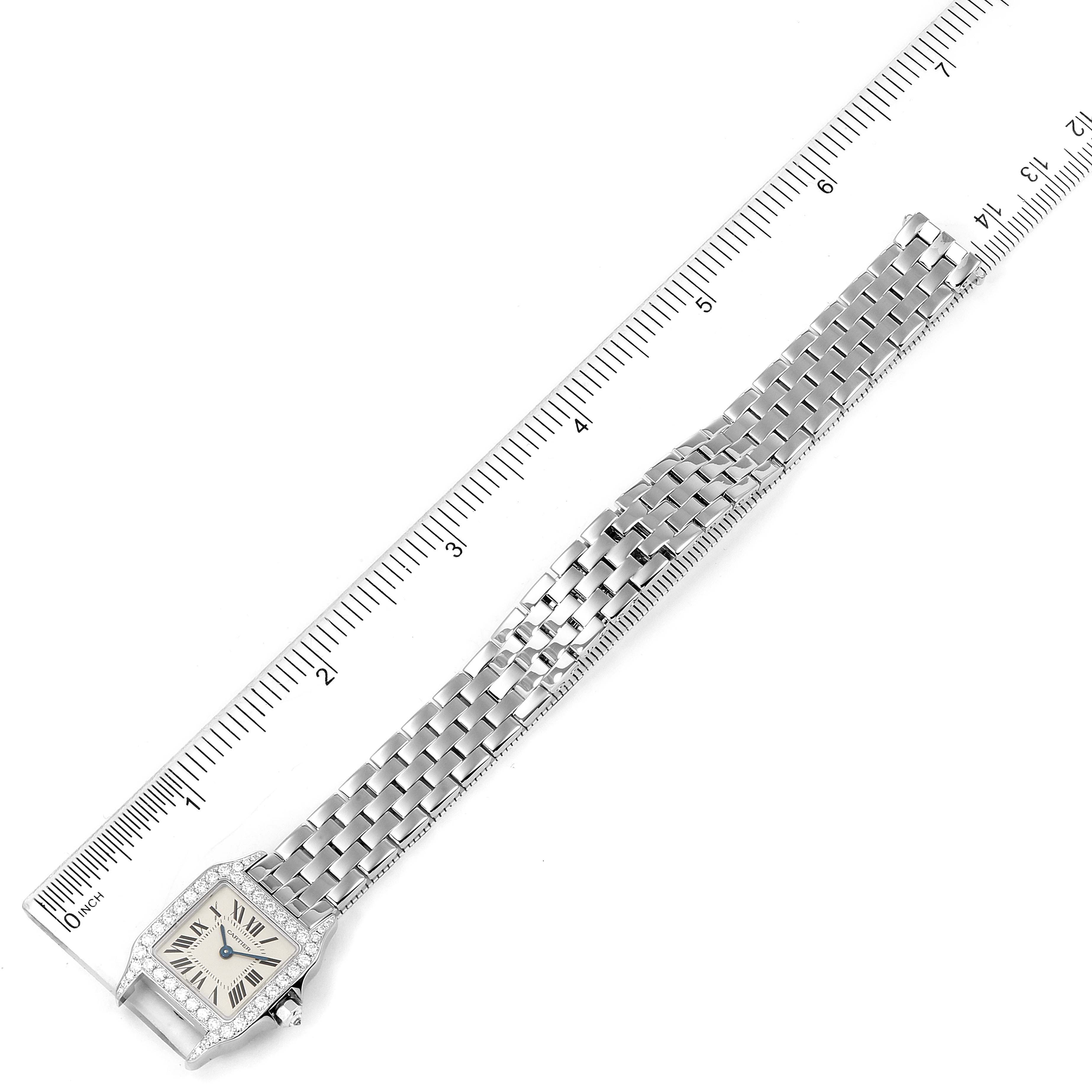The Cartier Santos Demoiselle WF9005Y8 Women's White Gold Silver Dial WF9005Y8 Women's White Gold Silver Dial watch is shown from a top-down angle, including its face, bracelet, and a ruler for scale.