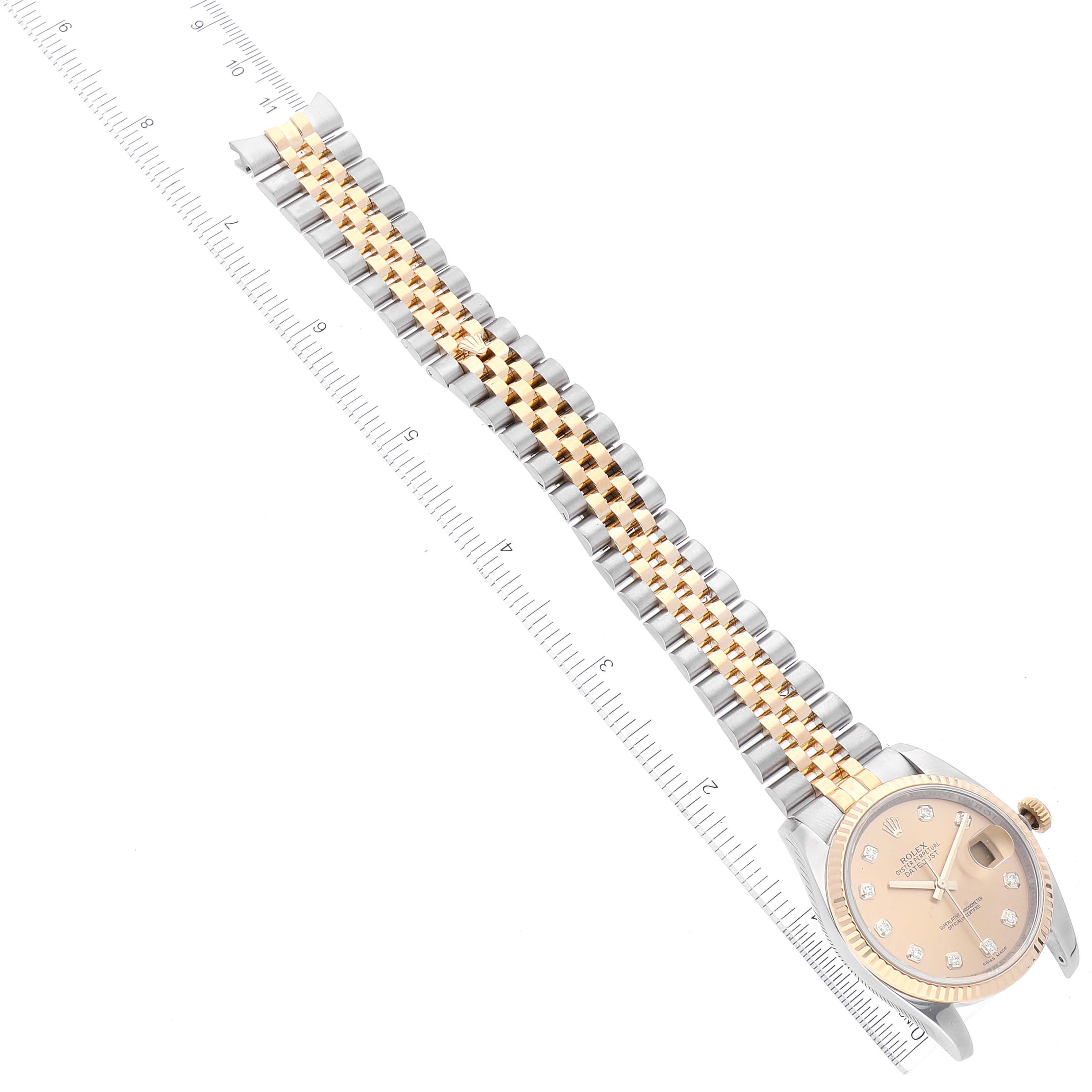 The image shows a top view of a Rolex Datejust 116233 Men's Steel and Gold (two tone) Champagne Dial 116233 Men's Steel and Gold (two tone) Champagne Dial watch, focusing on the face, and bracelet next to a measuring scale.