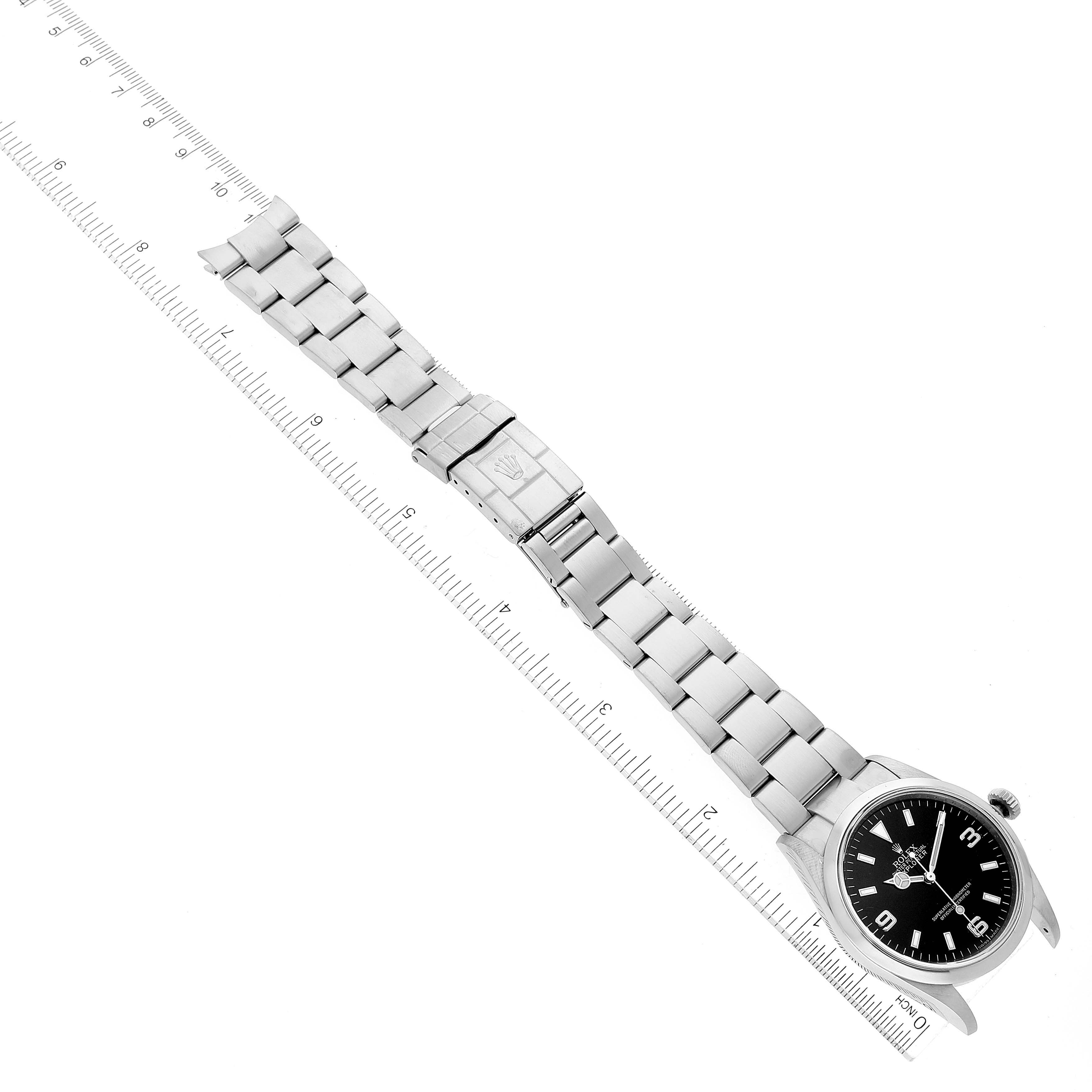 The image shows the Rolex Explorer 114270 Men
s Stainless Steel Black Dial 114270 Men
s Stainless Steel Black Dial watch at a slight diagonal angle, displaying the face, bracelet, and clasp next to a ruler for scale.