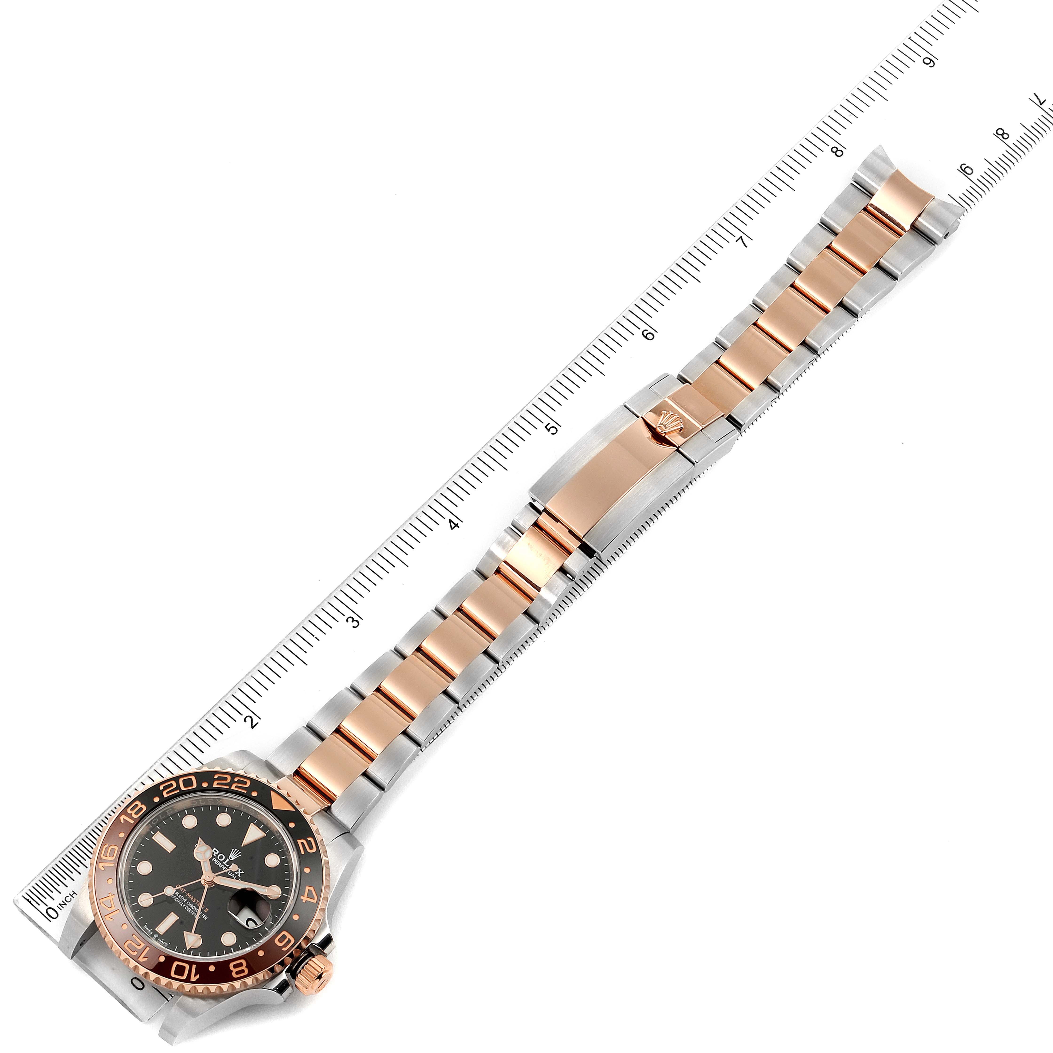 The image shows a Rolex GMT-Master 126711 Men
s Rose Gold Black Dial 126711 Men
s Rose Gold Black Dial watch placed diagonally across a ruler, highlighting its face, bezel, and bracelet.
