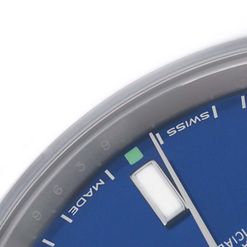 The image shows a close-up of the dial on a Rolex Oyster Perpetual 114300 Men's Stainless Steel Blue Dial 114300 Men's Stainless Steel Blue Dial, focusing on the hour markers and part of the bezel.