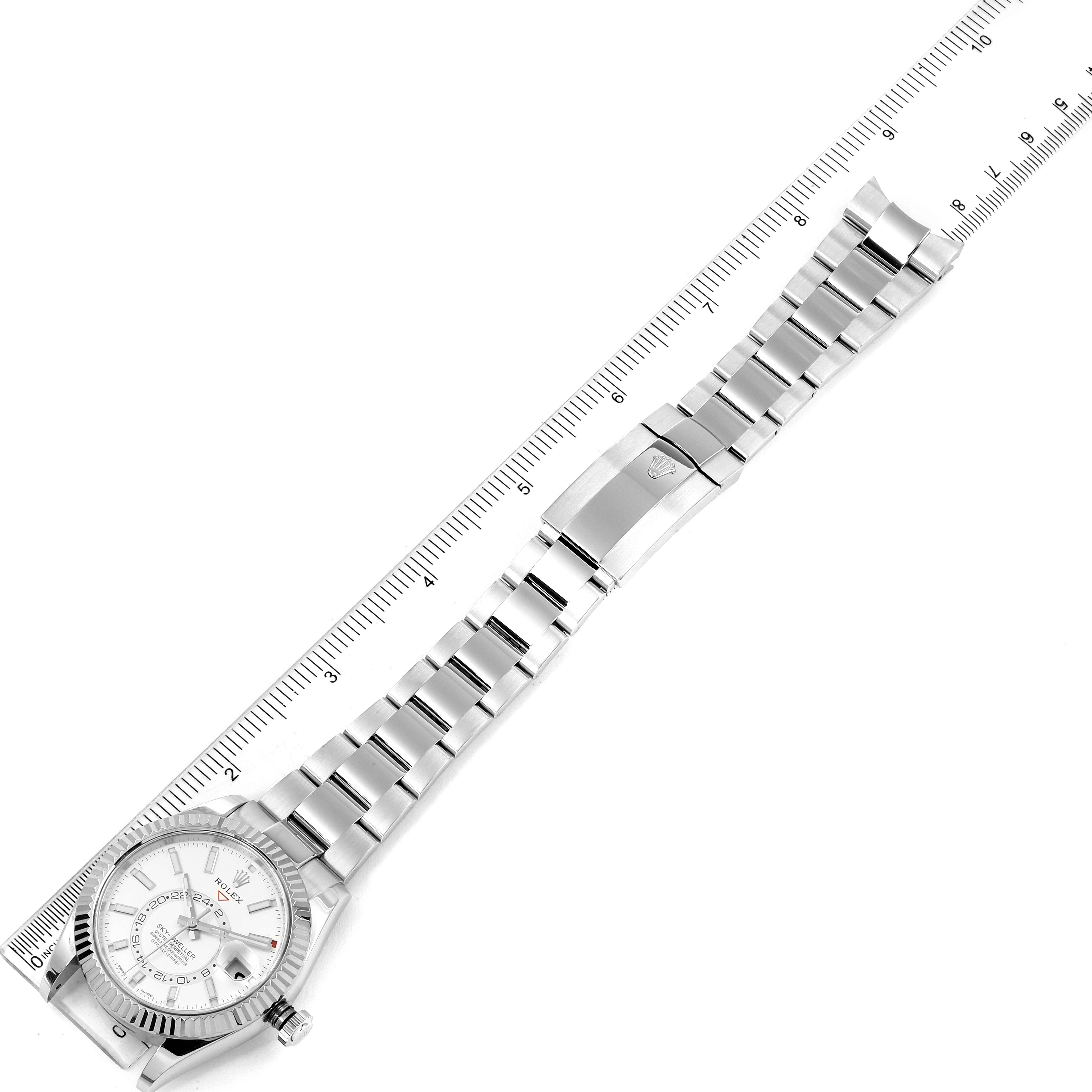 The image shows a top-down view of the Rolex Sky-Dweller 326934 Men's Stainless Steel White Dial 326934 Men's Stainless Steel White Dial watch, including its face, bracelet, and clasp adjacent to a ruler.