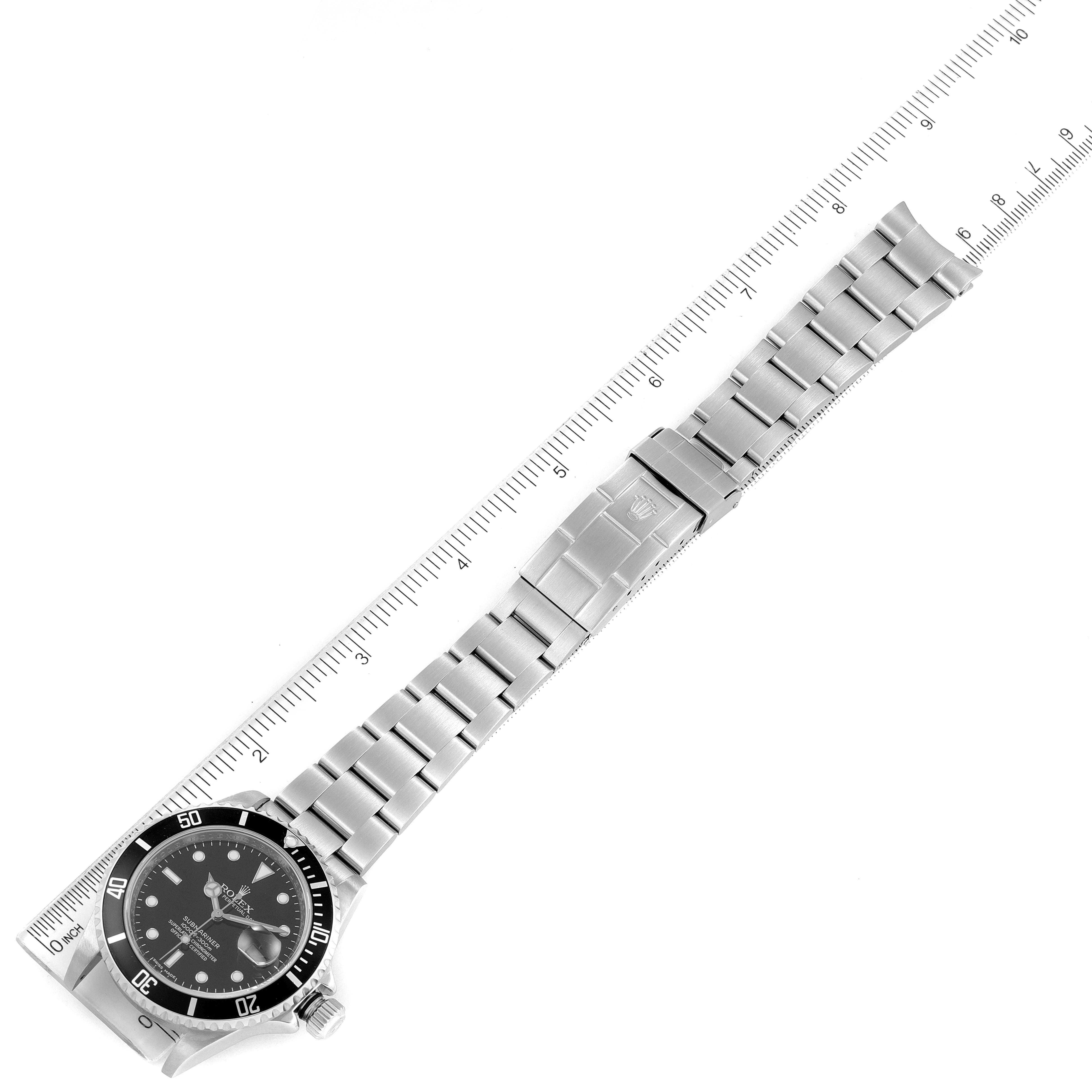 The image shows a flat-lay view of a Rolex Submariner 16610 Men
s Stainless Steel Black Dial 16610 Men
s Stainless Steel Black Dial watch including both the face and band, next to a ruler for scale.