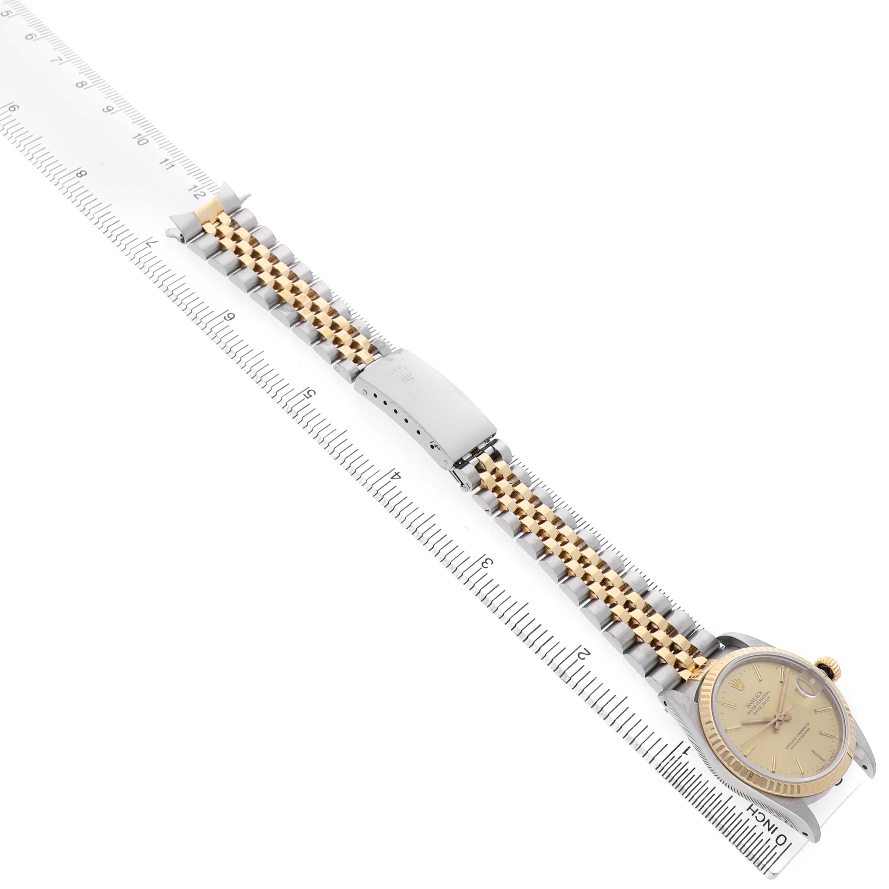 The Rolex Datejust 68273 Women's Steel and Gold (two tone) Champagne Dial watch is shown from a top angle, highlighting the face, bezel, and two-tone bracelet against a ruler.