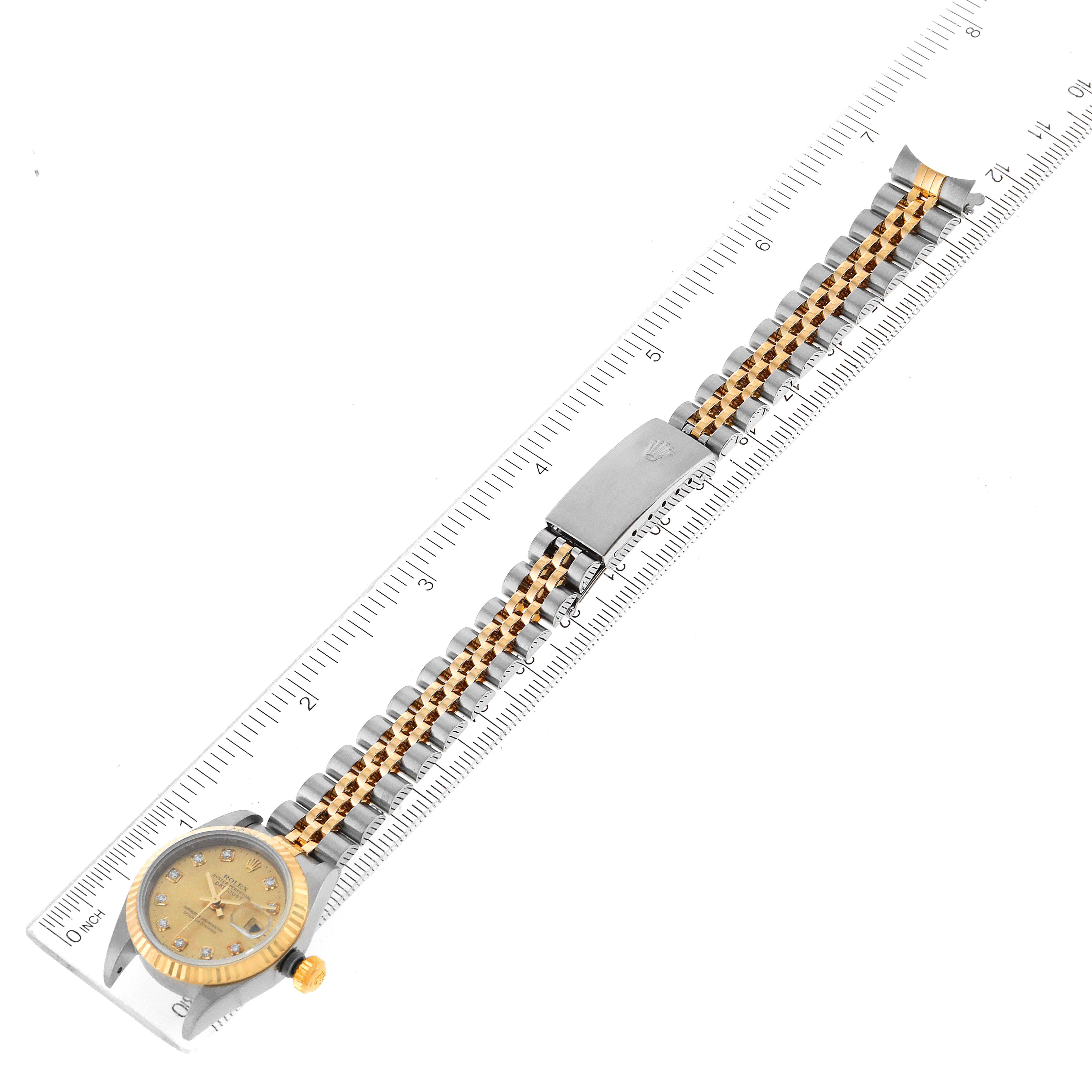 This image shows a Rolex Datejust 79173 Women
s Steel and Gold (two tone) Champagne Dial 79173 Women
s Steel and Gold (two tone) Champagne Dial watch placed diagonally against a ruler, displaying its face, crown, bezel, and bracelet.