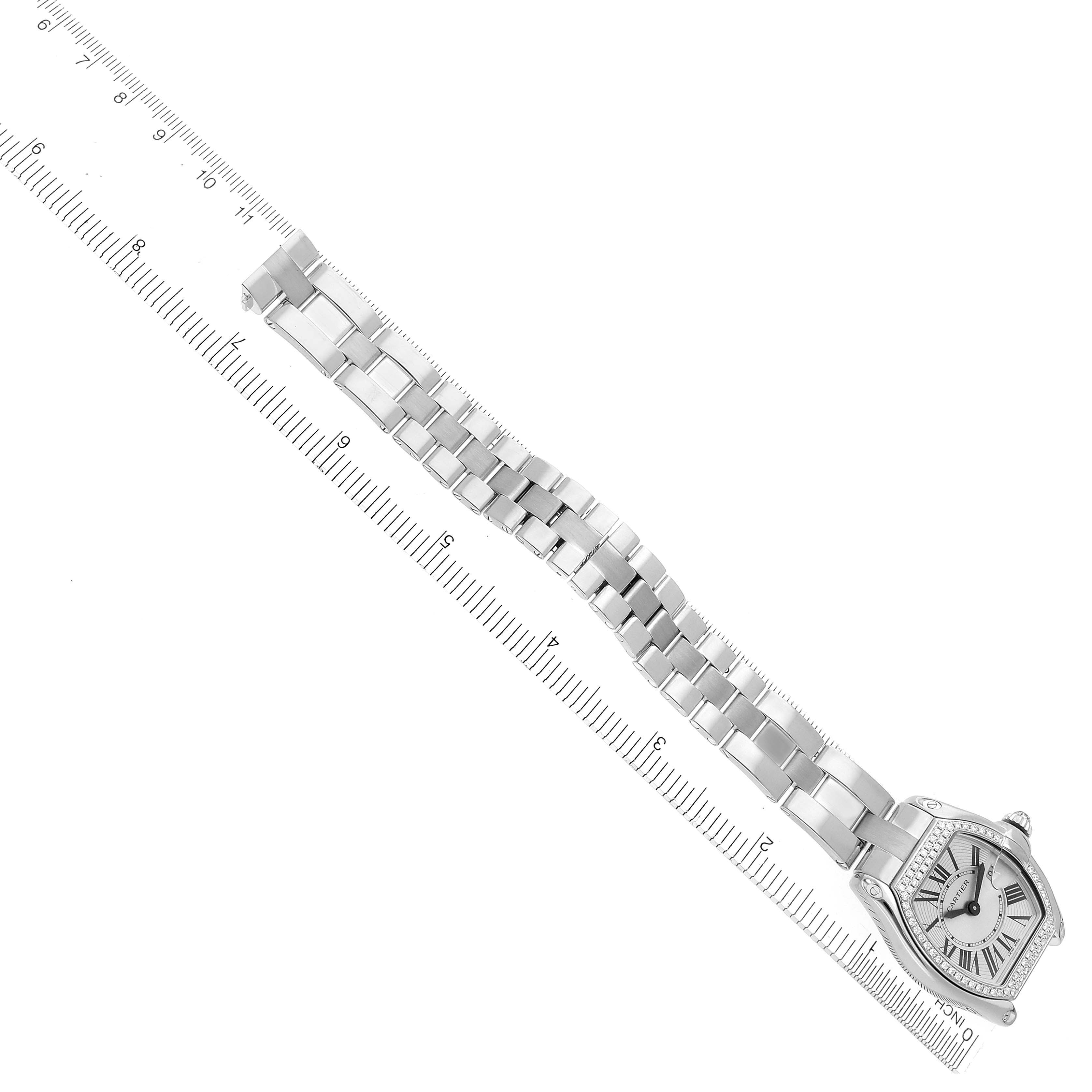 The Cartier Roadster WE5002X2 Women
s White Gold Silver Dial WE5002X2 Women
s White Gold Silver Dial watch is shown diagonally, highlighting its face and bracelet against a ruler for scale.
