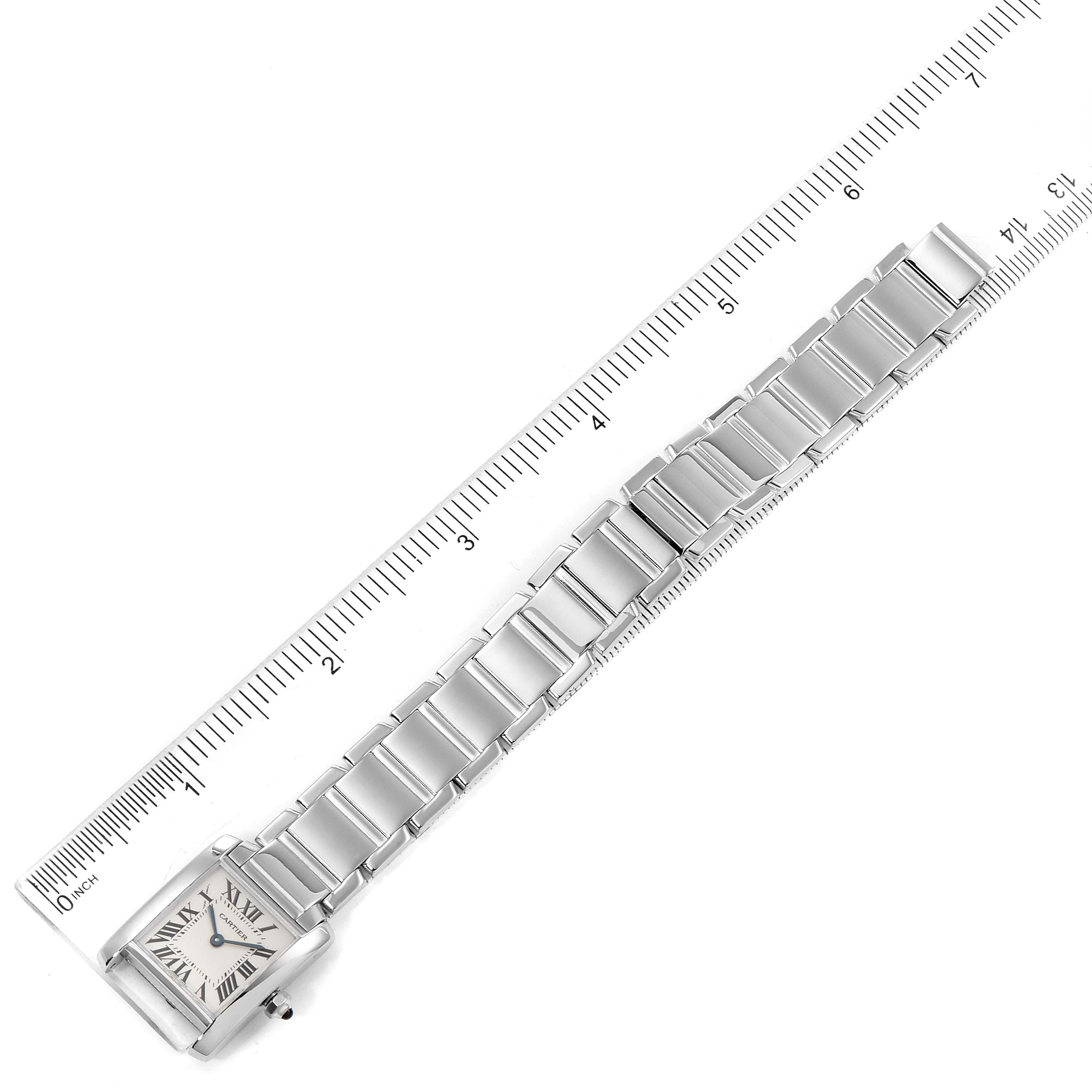 The image shows an overhead view of a Cartier Tank Francaise W50012S3 Women's White Gold Silver Dial W50012S3 Women's White Gold Silver Dial watch, highlighting its bracelet and square face alongside a ruler for scale.