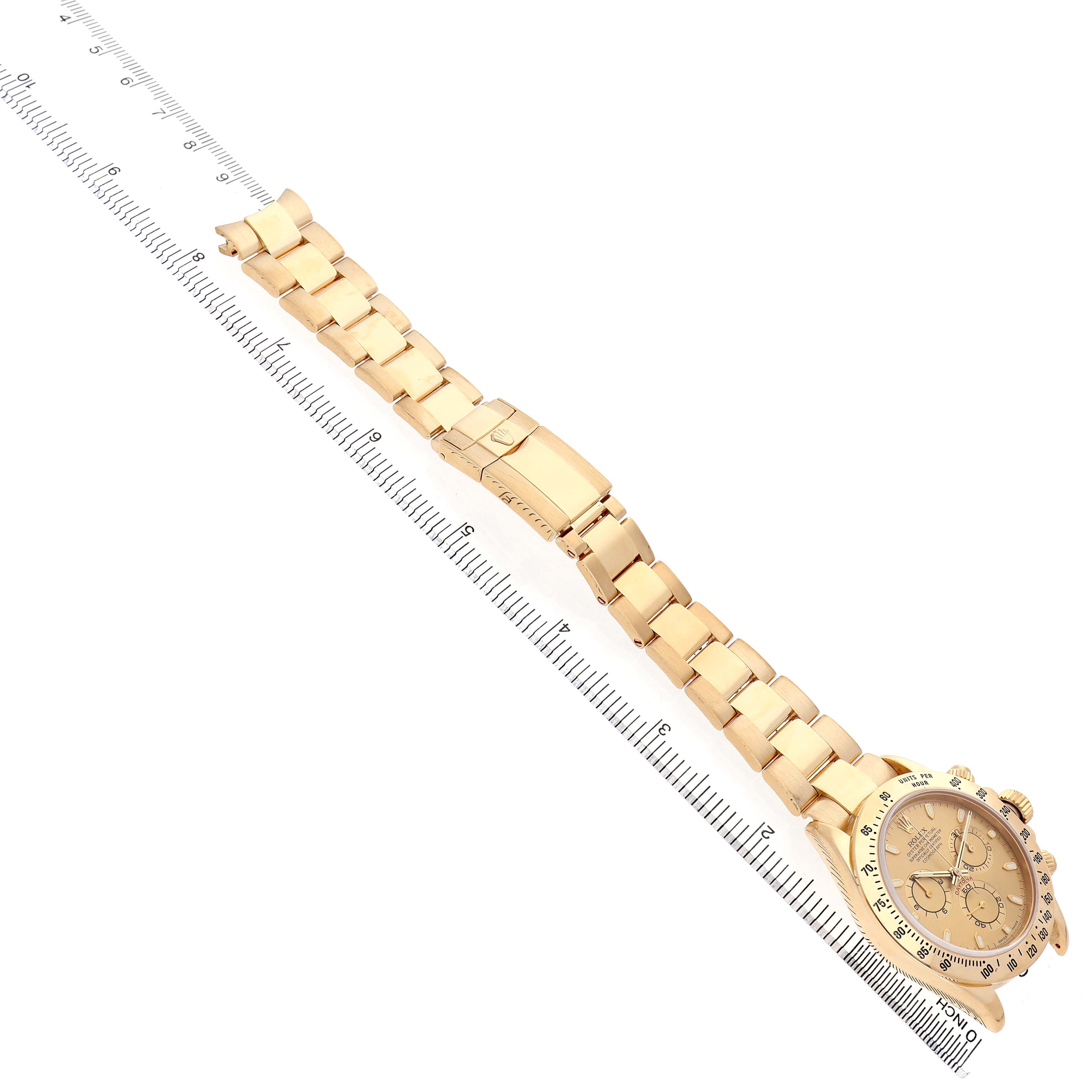 The Rolex Daytona 116528 Men's Yellow Gold Champagne Dial watch is shown from an angled top view, highlighting its gold bracelet and clasp alongside a measuring ruler.
