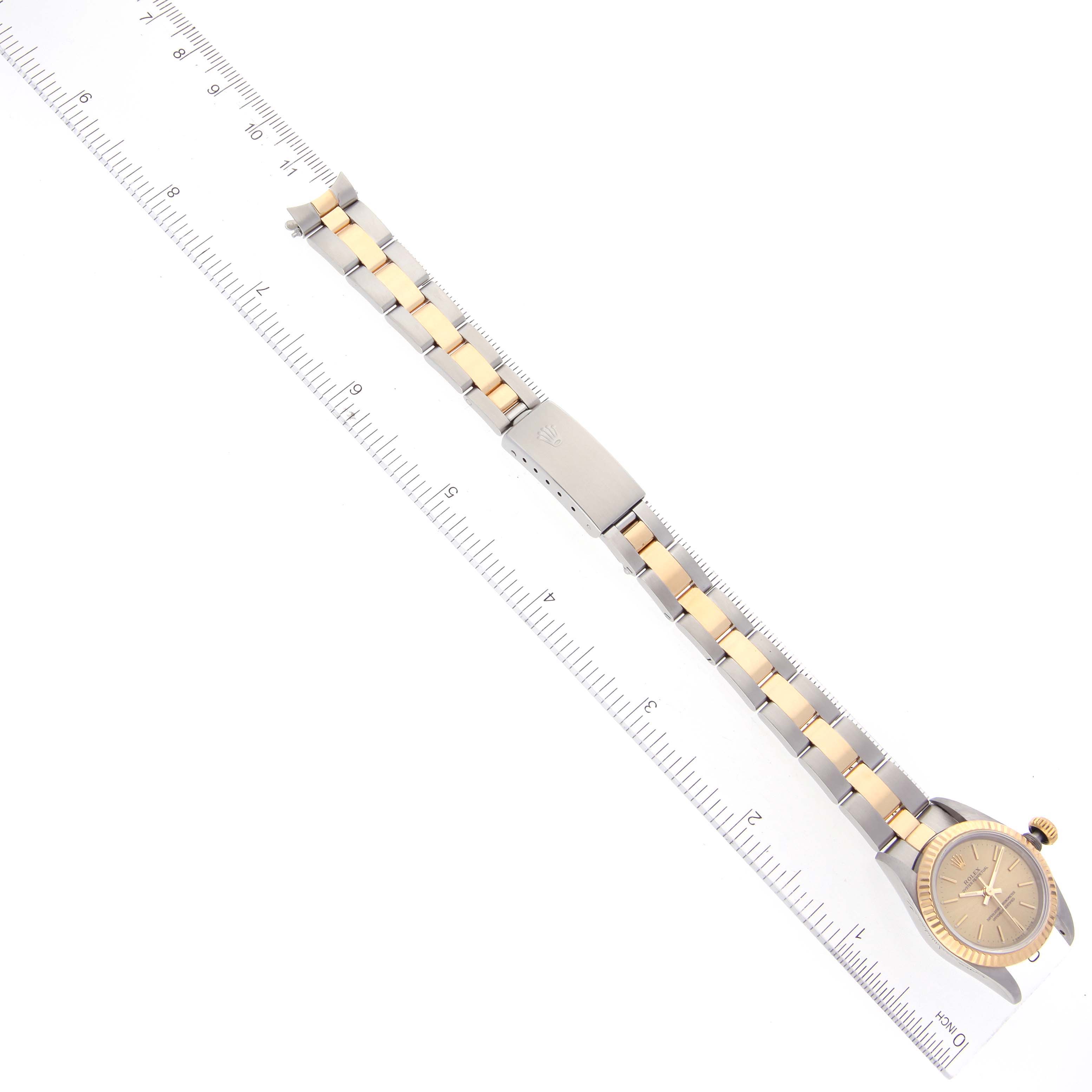 This image shows a top-down view of a Rolex Oyster Perpetual 67193 Women's Steel and Gold (two tone) Champagne Dial 67193 Women's Steel and Gold (two tone) Champagne Dial watch with its bracelet extended alongside a ruler for scale.