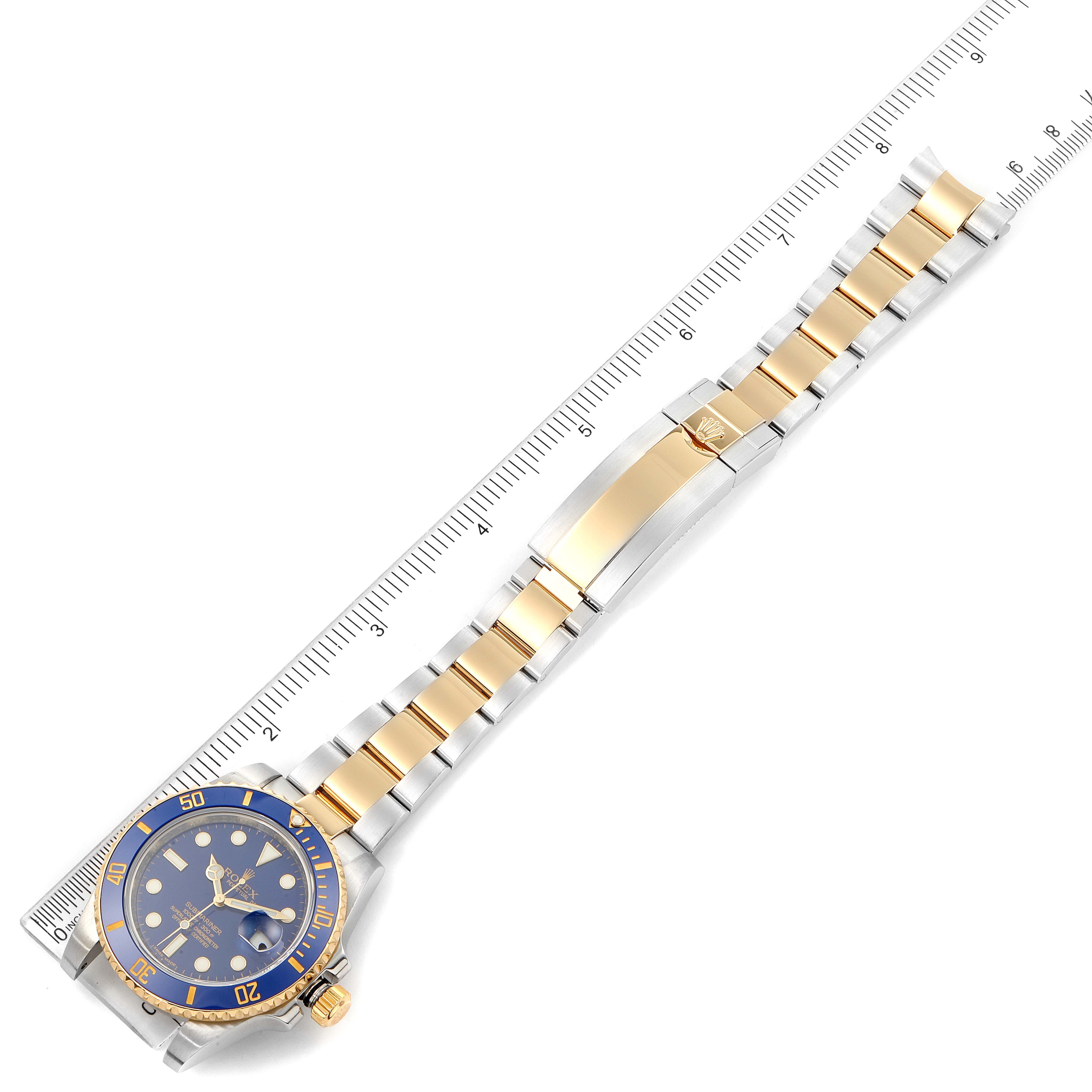 The image shows a Rolex Submariner 116613 Men's Steel and Gold (two tone) Blue Dial 116613 Men's Steel and Gold (two tone) Blue Dial watch with a blue and gold bezel, face, and bracelet laid flat next to a ruler.