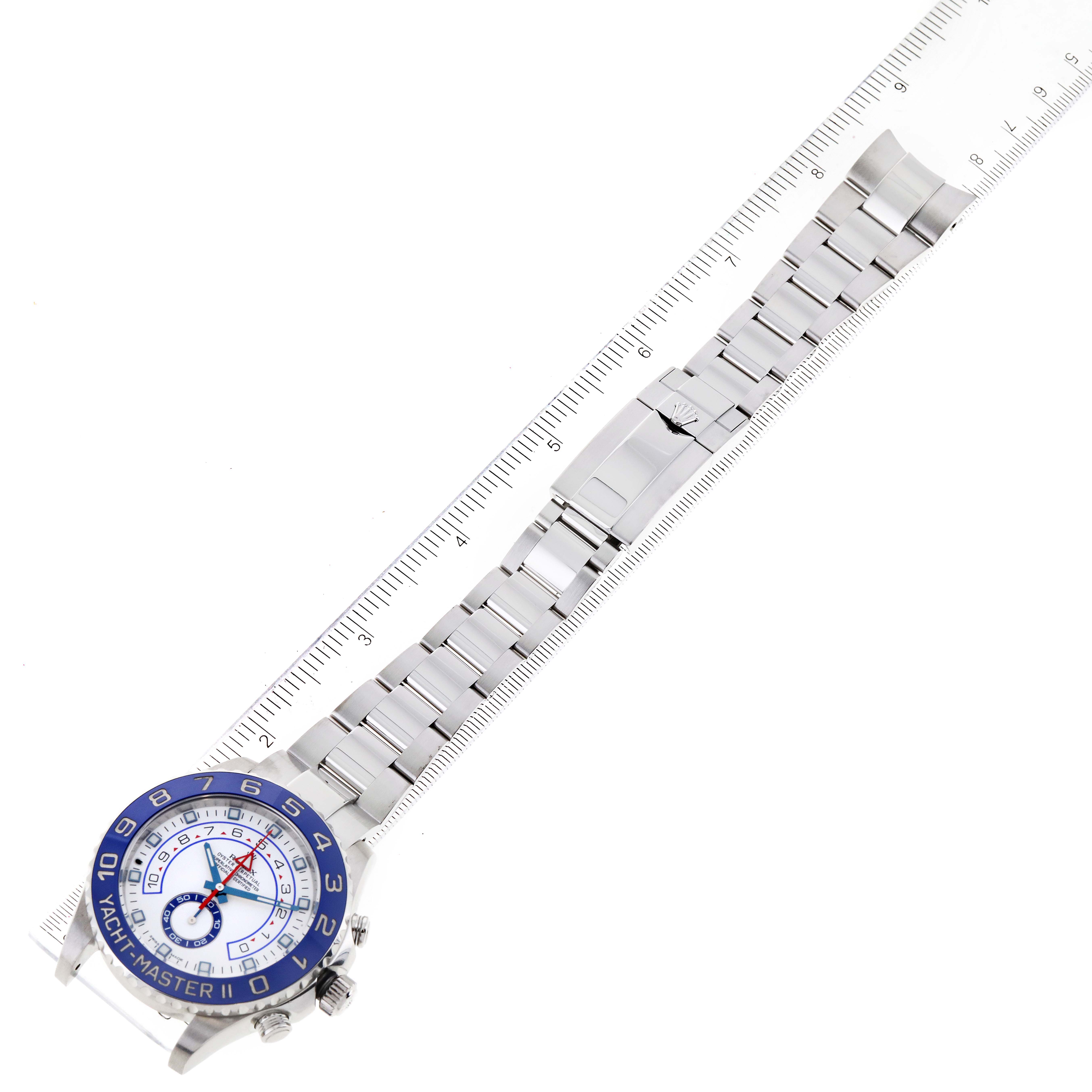 The image shows an overhead view of a Rolex Yacht-Master 116680 Men's Stainless Steel White Dial 116680 Men's Stainless Steel White Dial watch laying flat with its bracelet extended alongside a ruler.