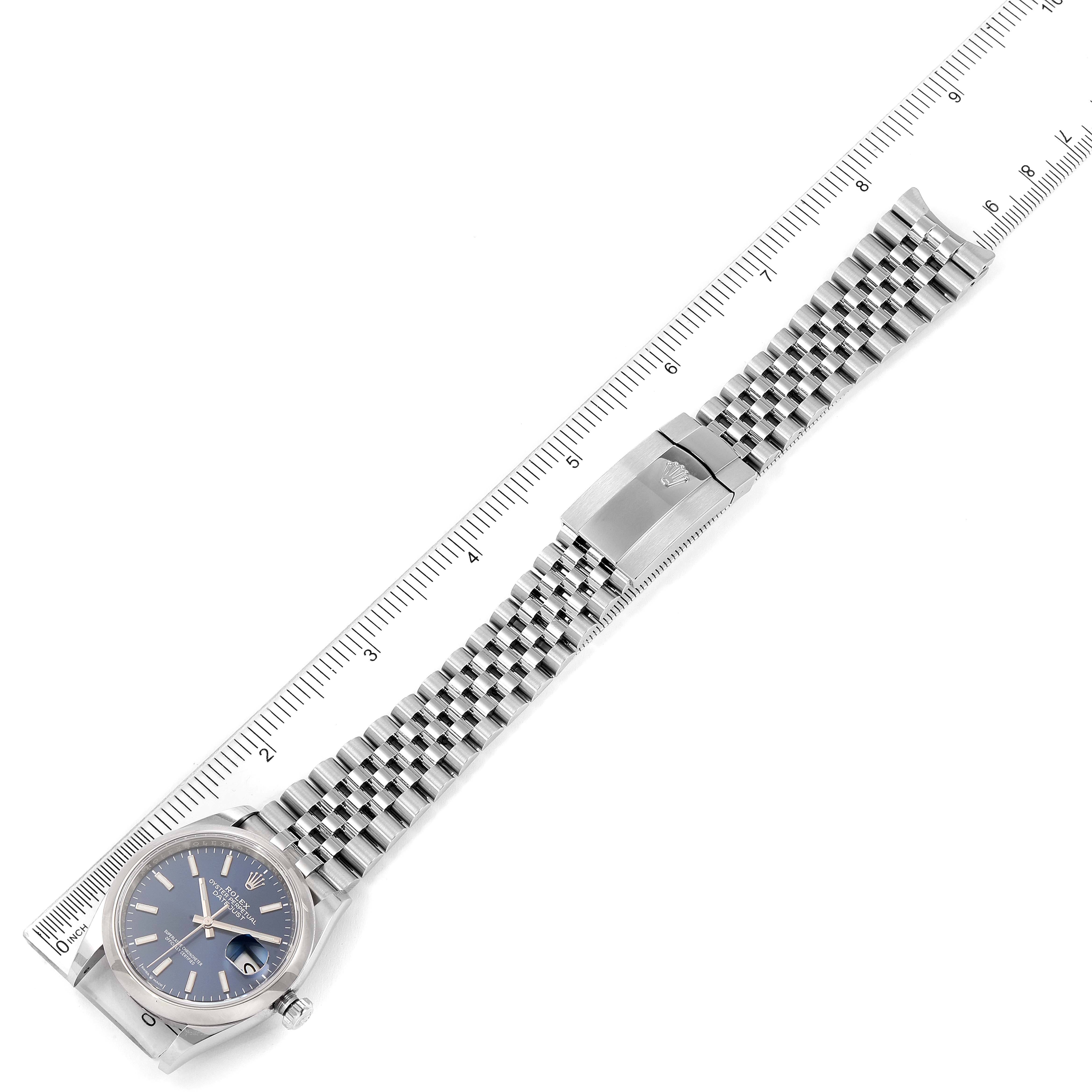 The Rolex Datejust 126200 Men's Stainless Steel Blue Dial 126200 Men's Stainless Steel Blue Dial watch is shown from a top-down angle, displaying the face, bracelet, and clasp alongside a ruler for scale.
