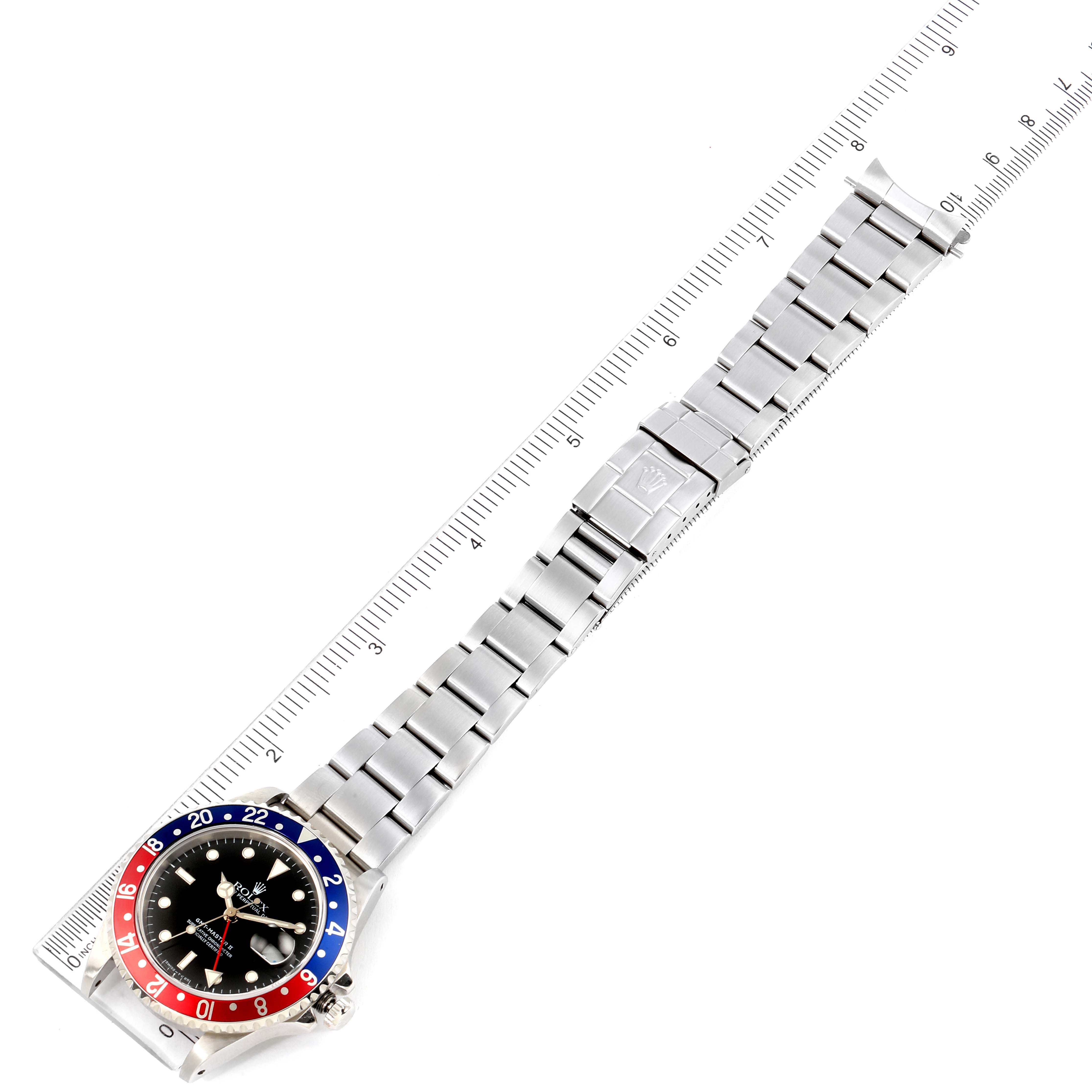 The Rolex GMT-Master 16710 Men
s Stainless Steel Black Dial 16710 Men
s Stainless Steel Black Dial watch is shown from an aerial view with its entire bracelet and bezel visible, alongside a measuring scale.