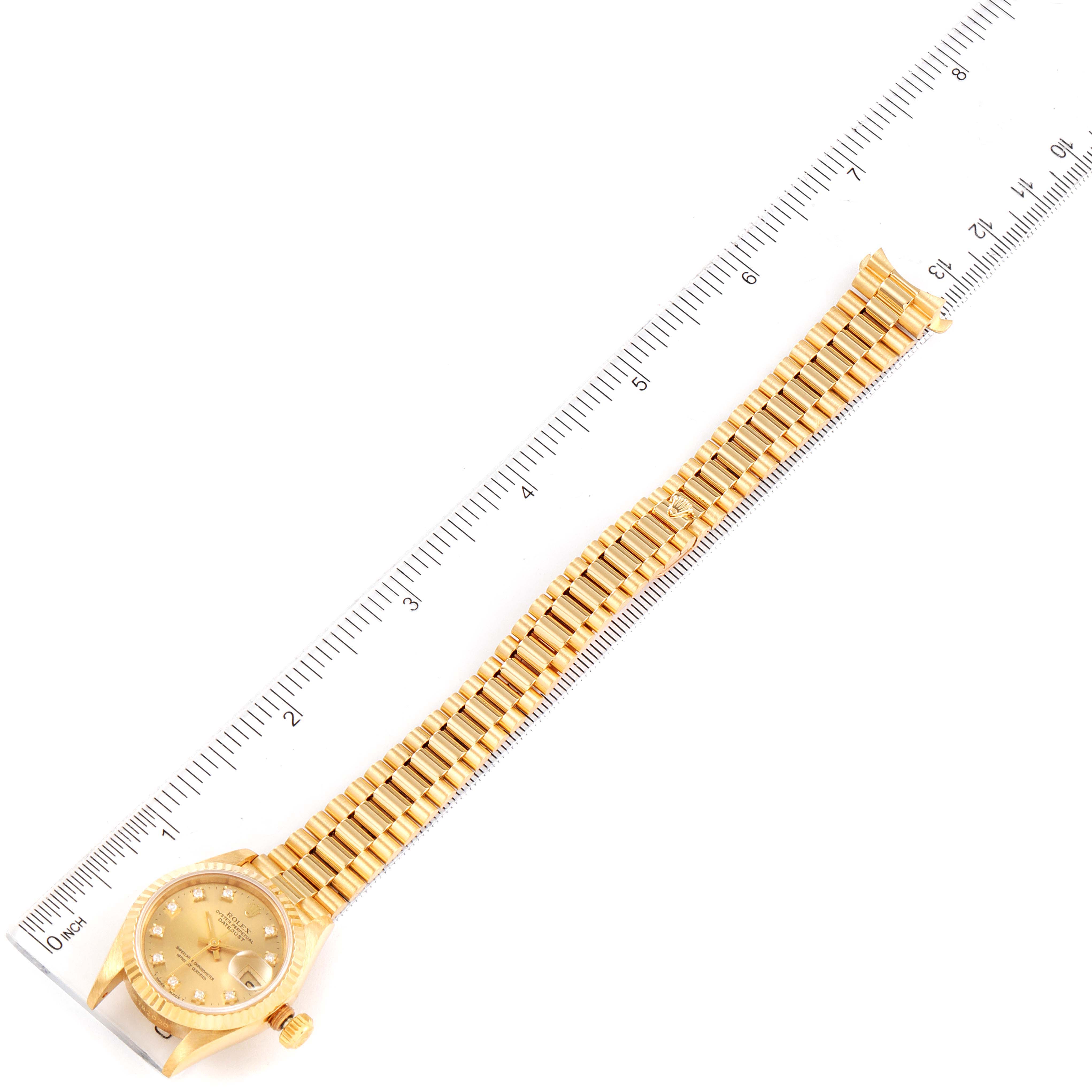 The image shows a top-down view of a Rolex President 69178 Women
s Yellow Gold Champagne Dial 69178 Women
s Yellow Gold Champagne Dial model watch with its band extended next to a ruler.