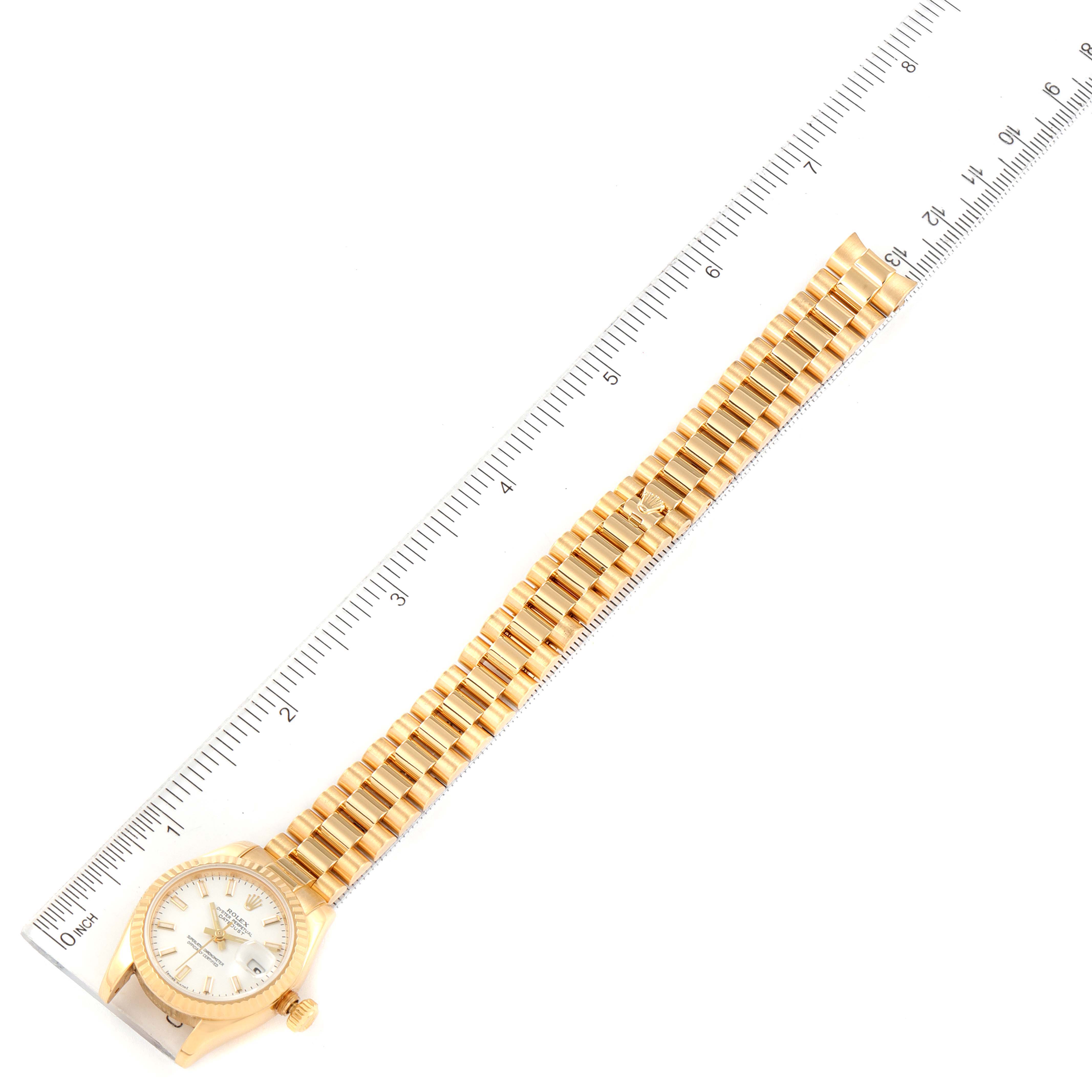 The image shows the full length of a gold Rolex President 179178 Women
s Yellow Gold White Dial 179178 Women
s Yellow Gold White Dial watch placed next to a ruler for scale.