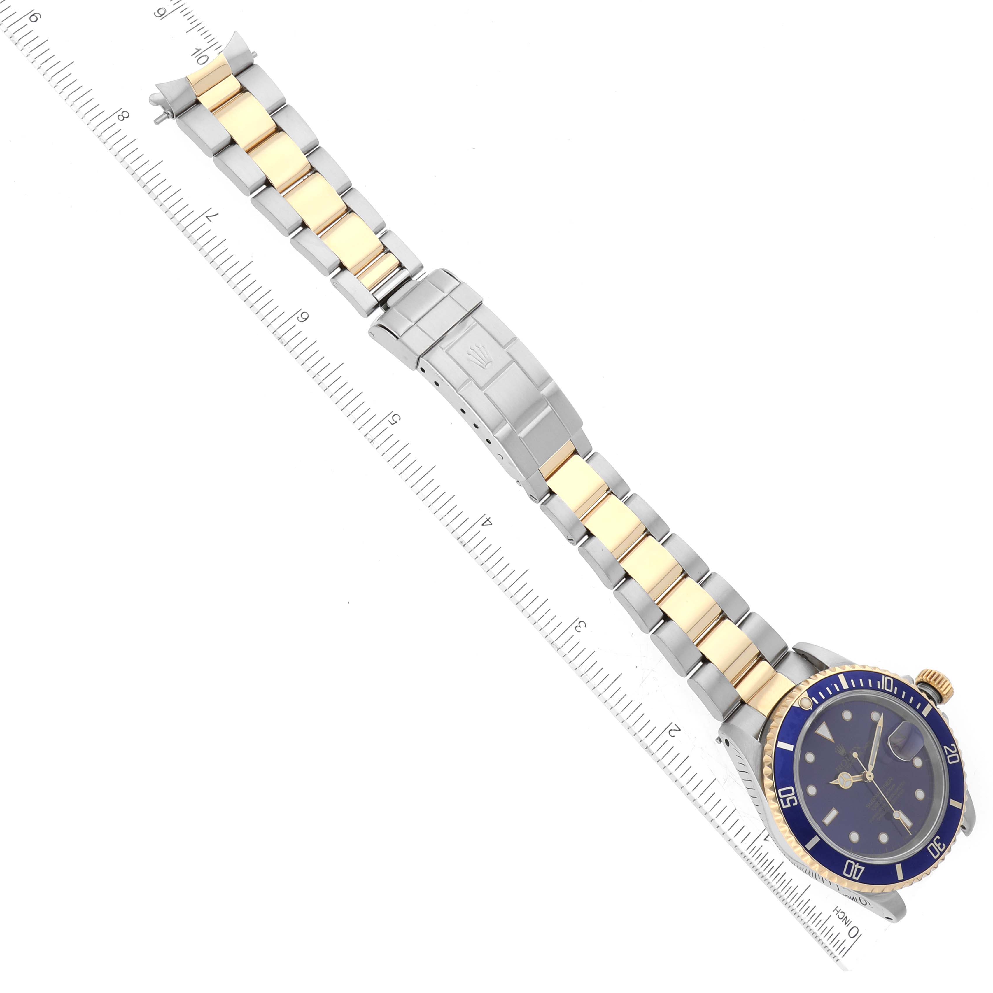 The image shows a Rolex Submariner 16613 Men
s Steel and Gold (two tone) Blue Dial 16613 Men
s Steel and Gold (two tone) Blue Dial watch with a blue bezel and gold accents, including the bracelet, displayed alongside a ruler.