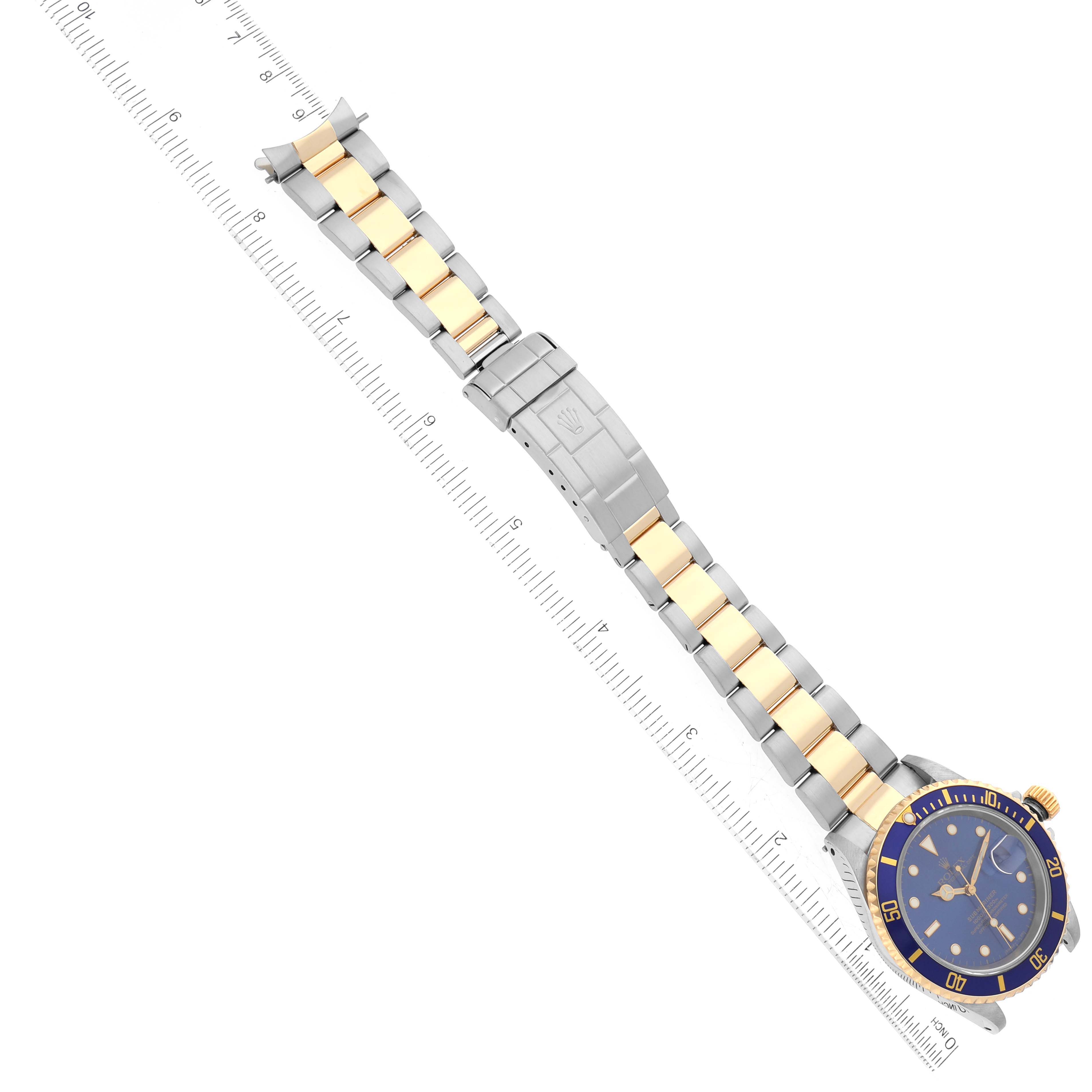 The Rolex Submariner 16613 Men
s Steel and Gold (two tone) Blue Dial 16613 Men
s Steel and Gold (two tone) Blue Dial watch is shown from a top-down view, highlighting the face, bezel, and bracelet alongside a measuring ruler.