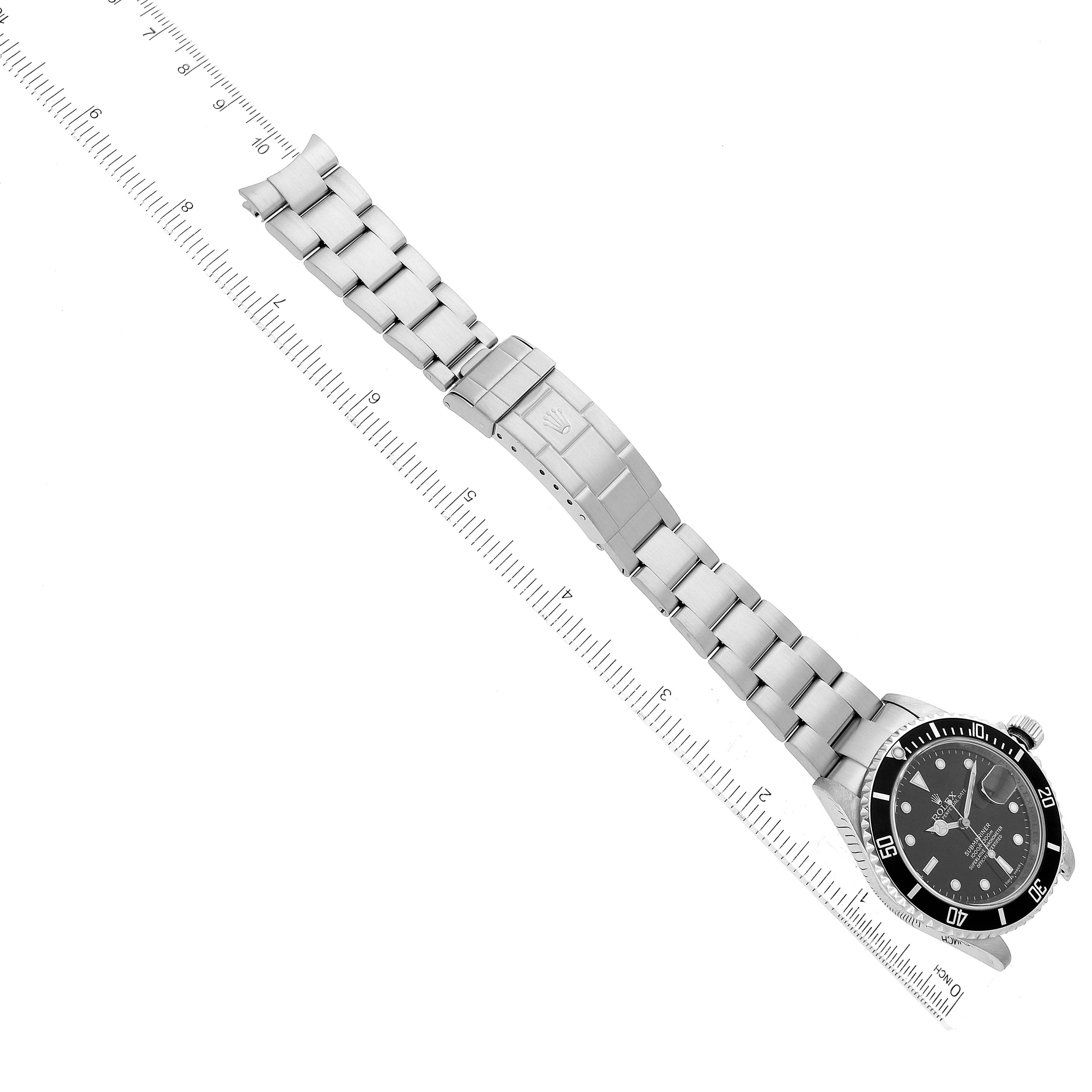 This image shows a top-down view of the Rolex Submariner 16610 Men
s Stainless Steel Black Dial 16610 Men
s Stainless Steel Black Dial watch, focusing on its face and metal bracelet with a ruler beside it.