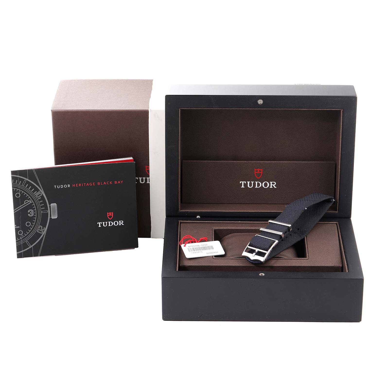 The image shows the packaging and accessories for the Tudor Heritage Black Bay 79230B Men's Stainless Steel Black Dial 79230B Men's Stainless Steel Black Dial watch, including a NATO strap and owner's booklet.