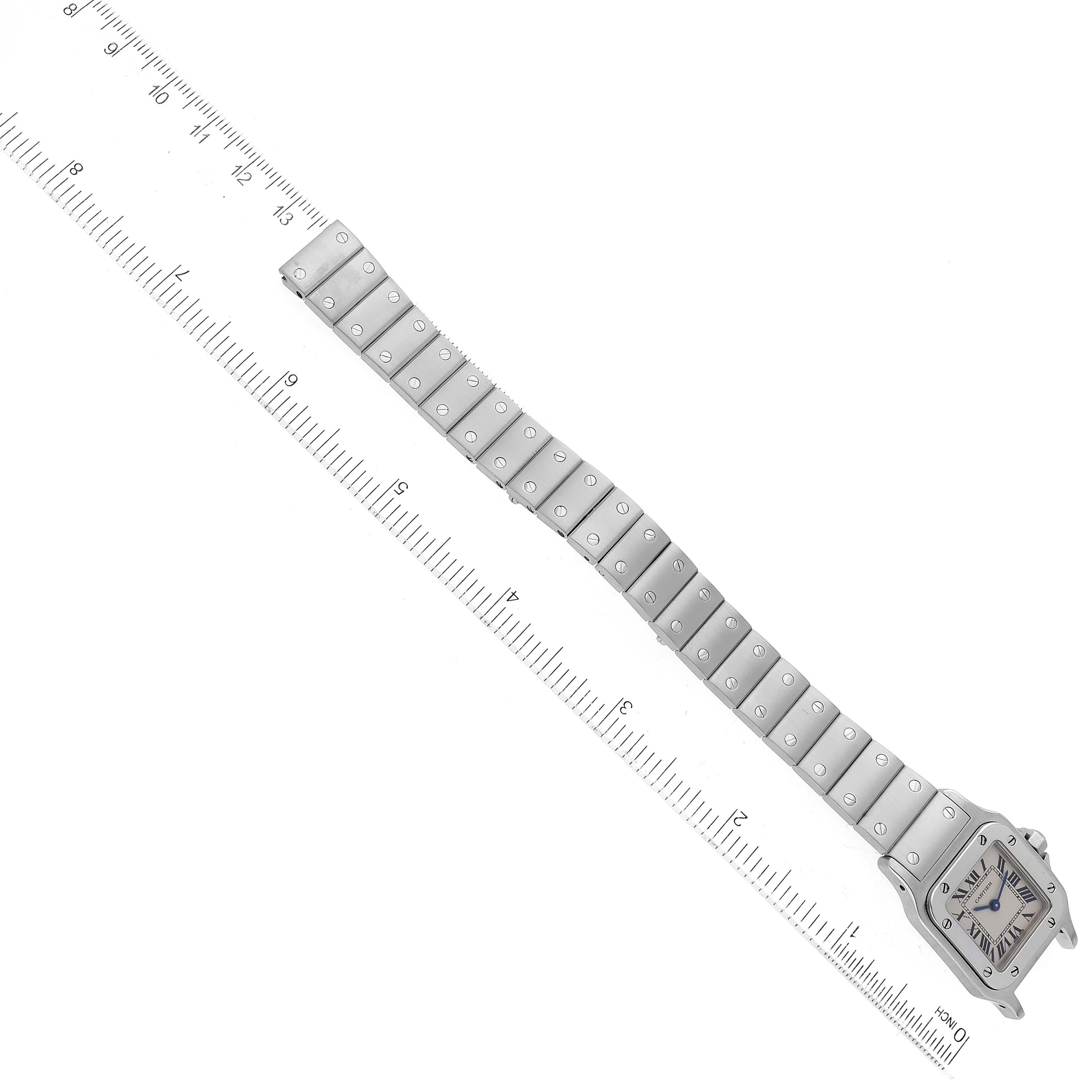 The Cartier Santos W20056D6 Women
s Stainless Steel Silver Dial W20056D6 Women
s Stainless Steel Silver Dial watch is shown from a top-down angle, displaying the face, bezel, and entire bracelet alongside a ruler for scale.