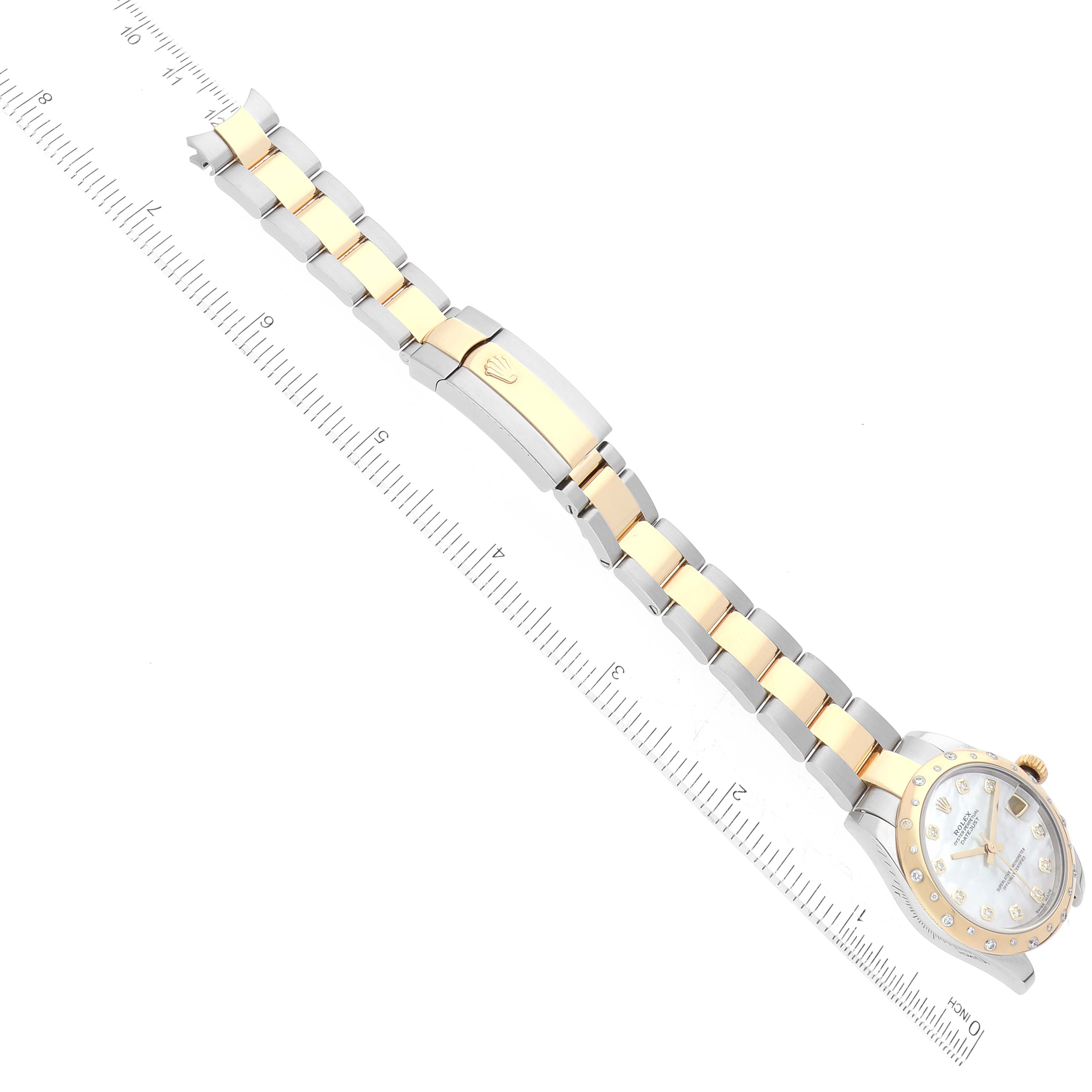 This image shows a Rolex Mid-Size 178343 Women
s Steel and Gold (two tone) Mother of Pearl Dial 178343 Women
s Steel and Gold (two tone) Mother of Pearl Dial model watch from an overhead angle, displaying the face, band, and clasp alongside a ruler.