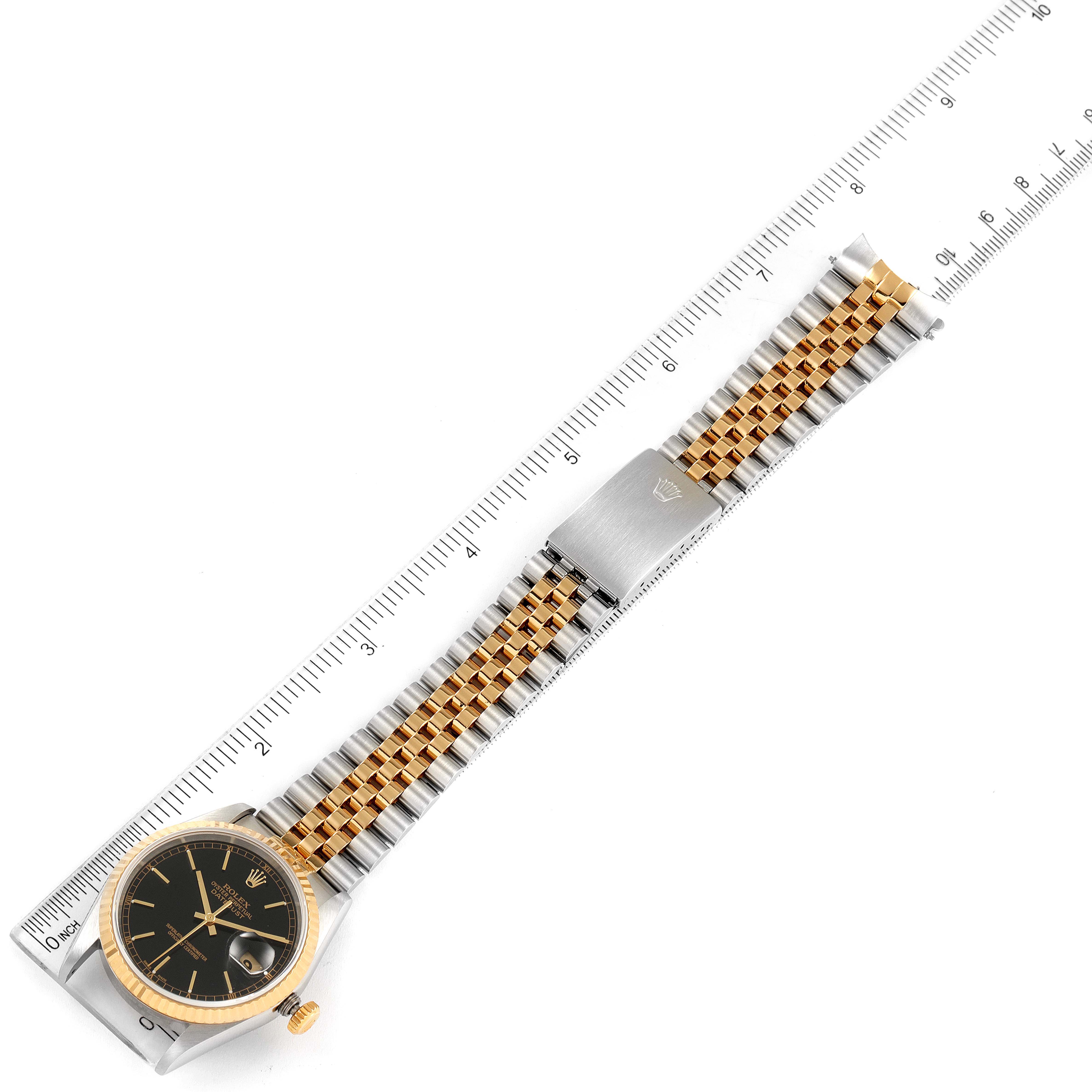The image shows a top-down view of a Rolex Datejust 16233 Men's Steel and Gold (two tone) Black Dial 16233 Men's Steel and Gold (two tone) Black Dial watch with a black dial, gold bezel, and two-tone bracelet, placed alongside a ruler for scale.