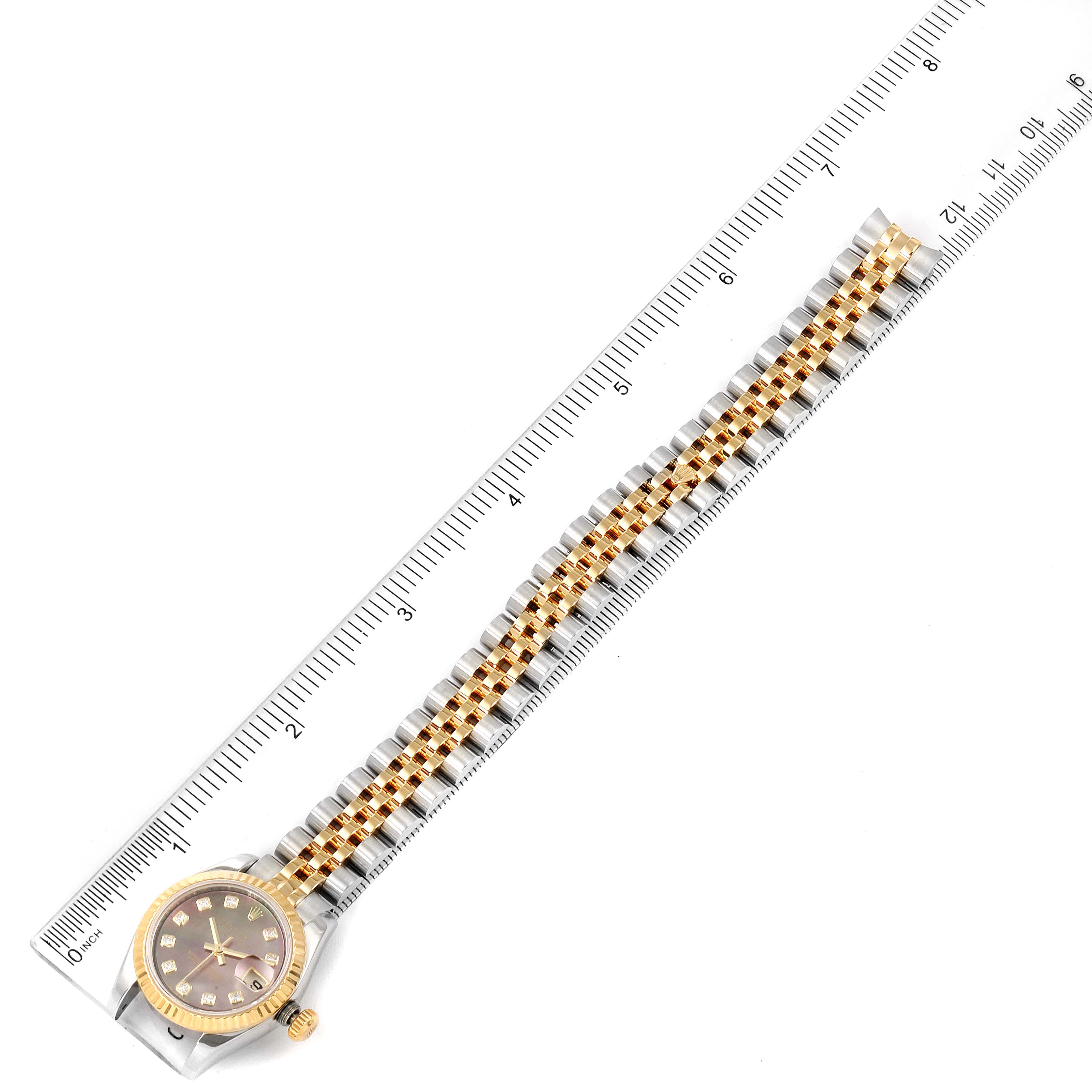 This Rolex Datejust 179173 Women's Steel and Gold (two tone) Mother of Pearl Dial 179173 Women's Steel and Gold (two tone) Mother of Pearl Dial watch is shown from a top-down angle, displaying the face, bezel, and full bracelet against a ruler for scale.