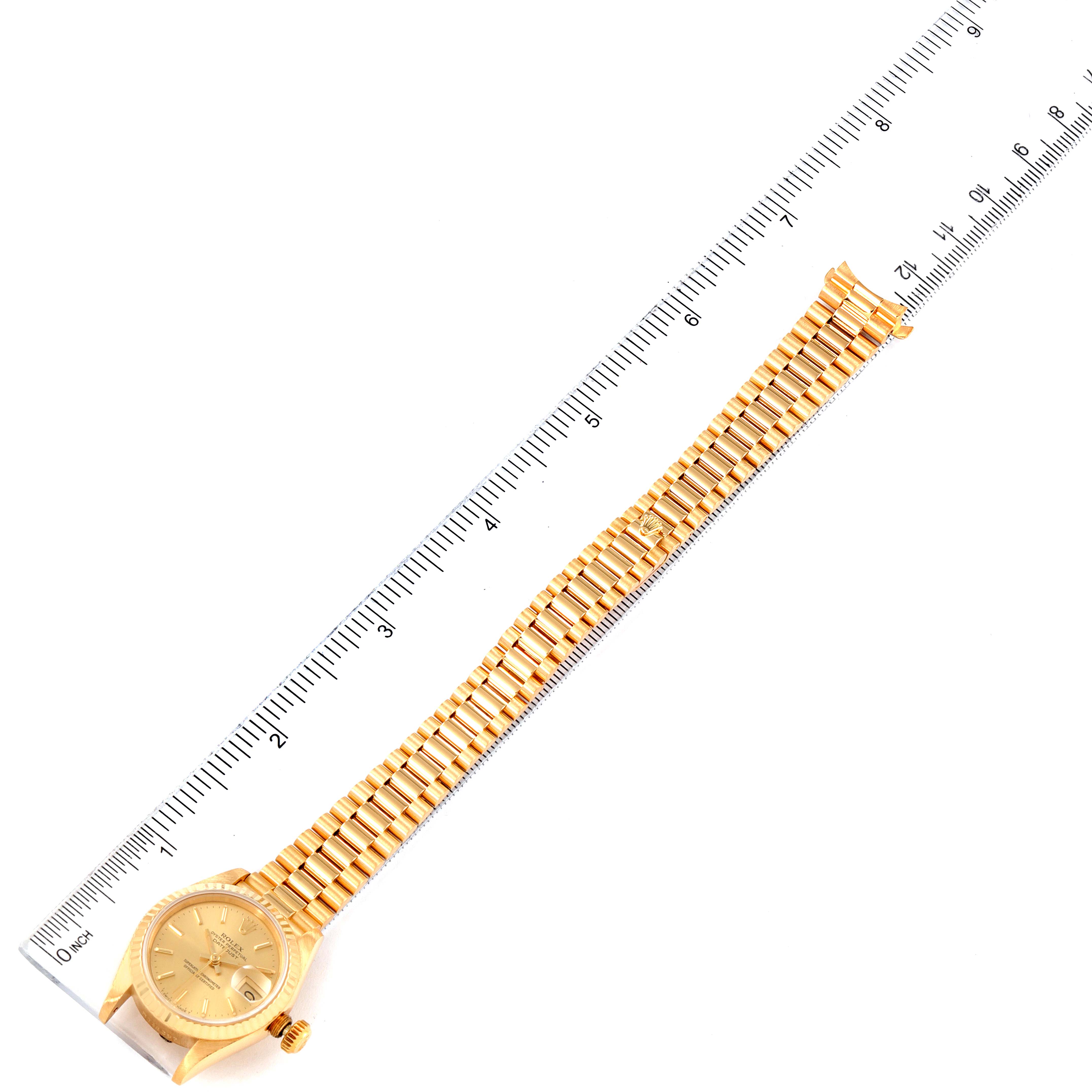 The Rolex President 69178 Women's Yellow Gold Champagne Dial 69178 Women's Yellow Gold Champagne Dial model watch is shown from a top-down angle, displaying its face, band, and crown placed next to a ruler.