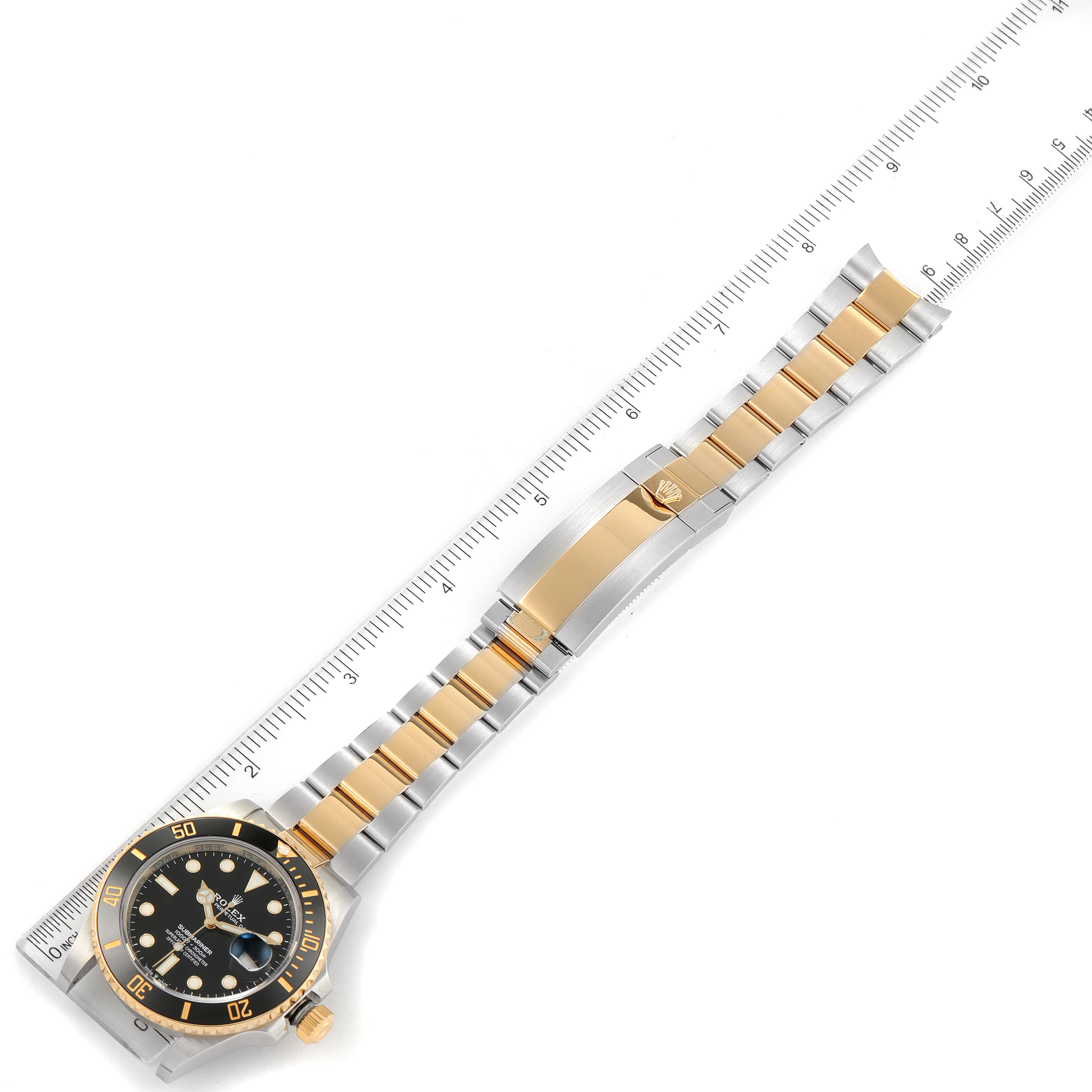 This image shows a Rolex Submariner 126613 Men's Steel and Gold (two tone) Black Dial 126613 Men's Steel and Gold (two tone) Black Dial watch laid flat with a ruler for scale, highlighting the bezel, dial, and bracelet.