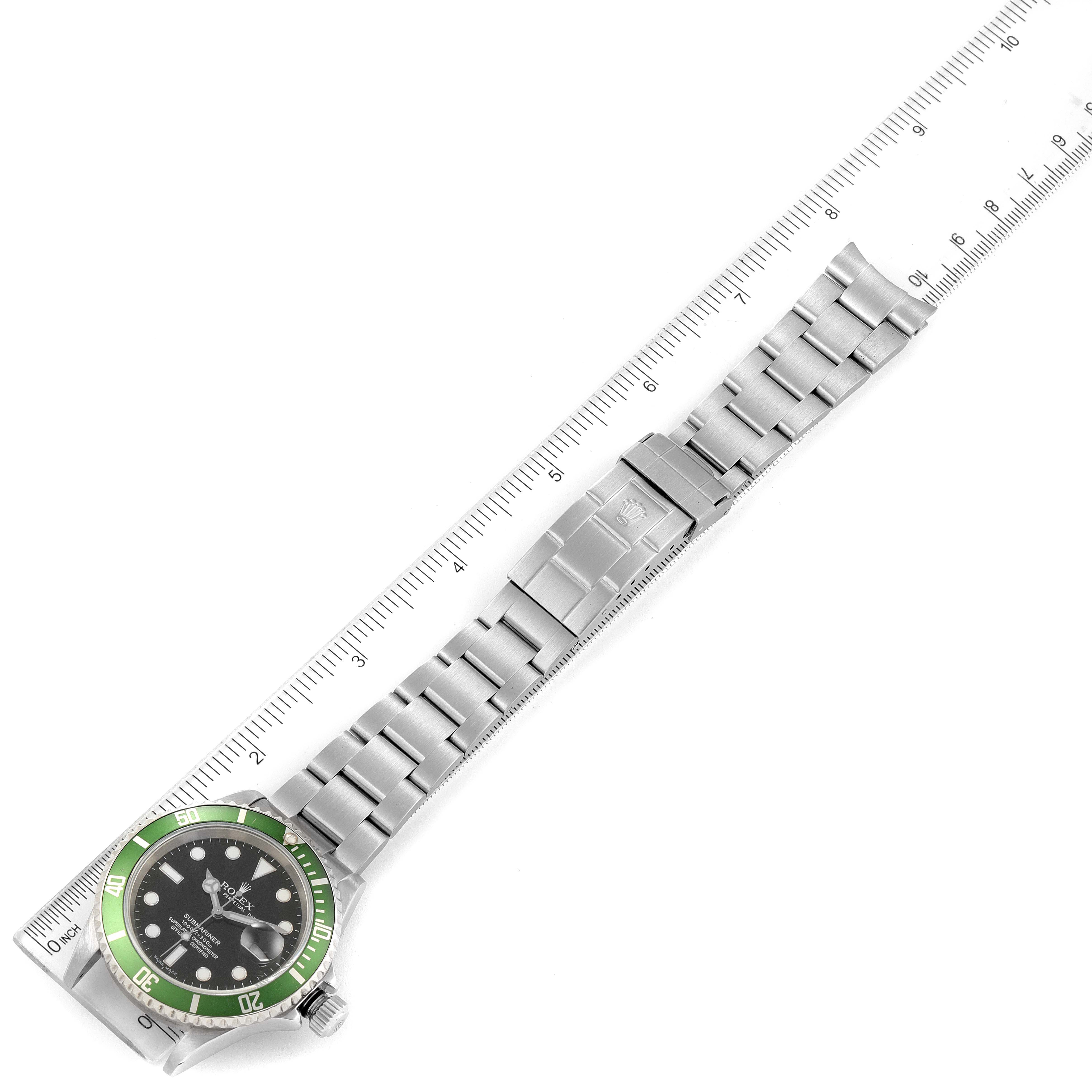 The image shows a Rolex Submariner 16610LV Men
s Stainless Steel Black Dial 16610LV Men
s Stainless Steel Black Dial watch laid flat with a green bezel, next to a ruler for measurement.