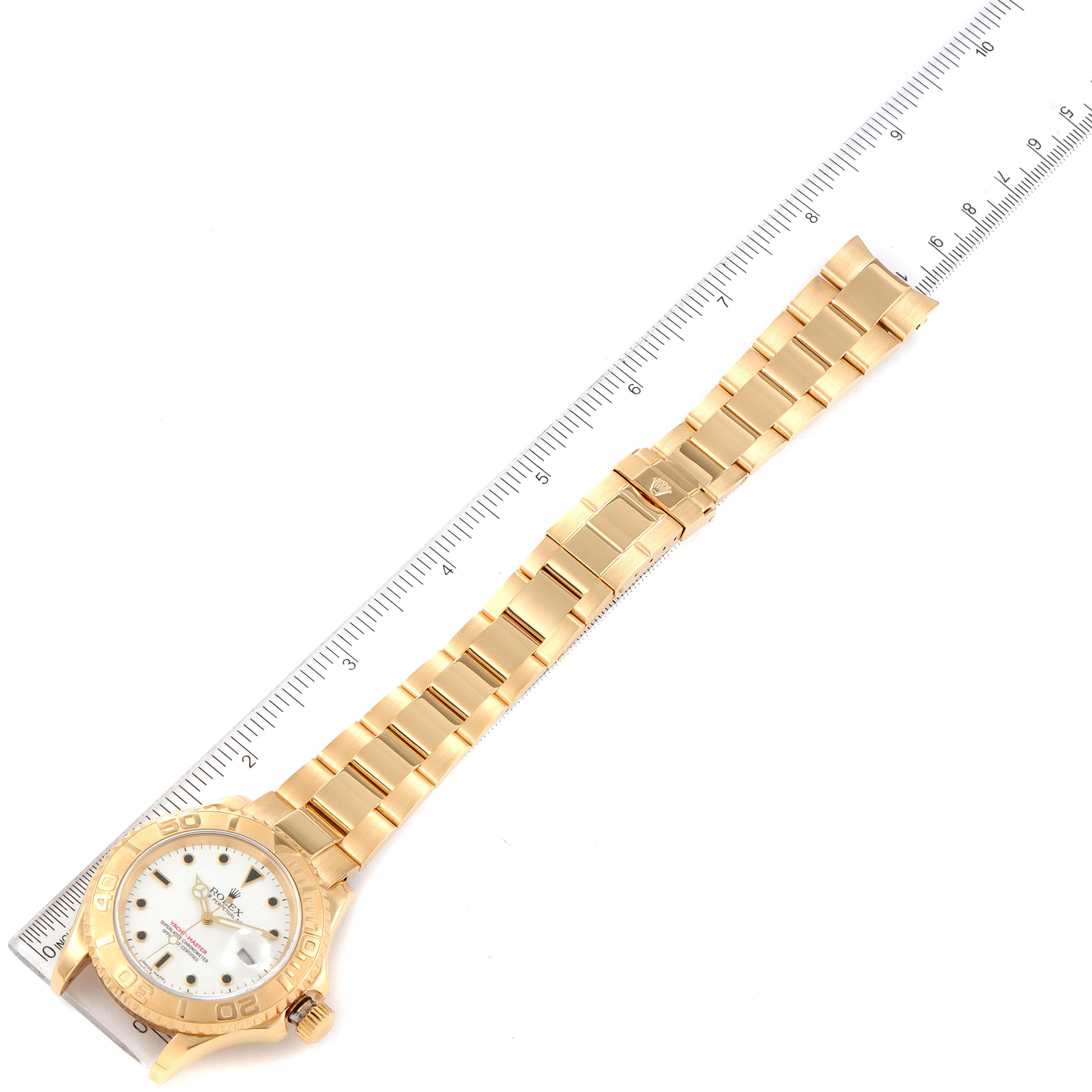 The image shows a full-length view of a Rolex Yacht-Master 16628 Men's Yellow Gold White Dial 16628 Men's Yellow Gold White Dial watch, including its face, bezel, bracelet, and clasp, positioned next to a ruler.