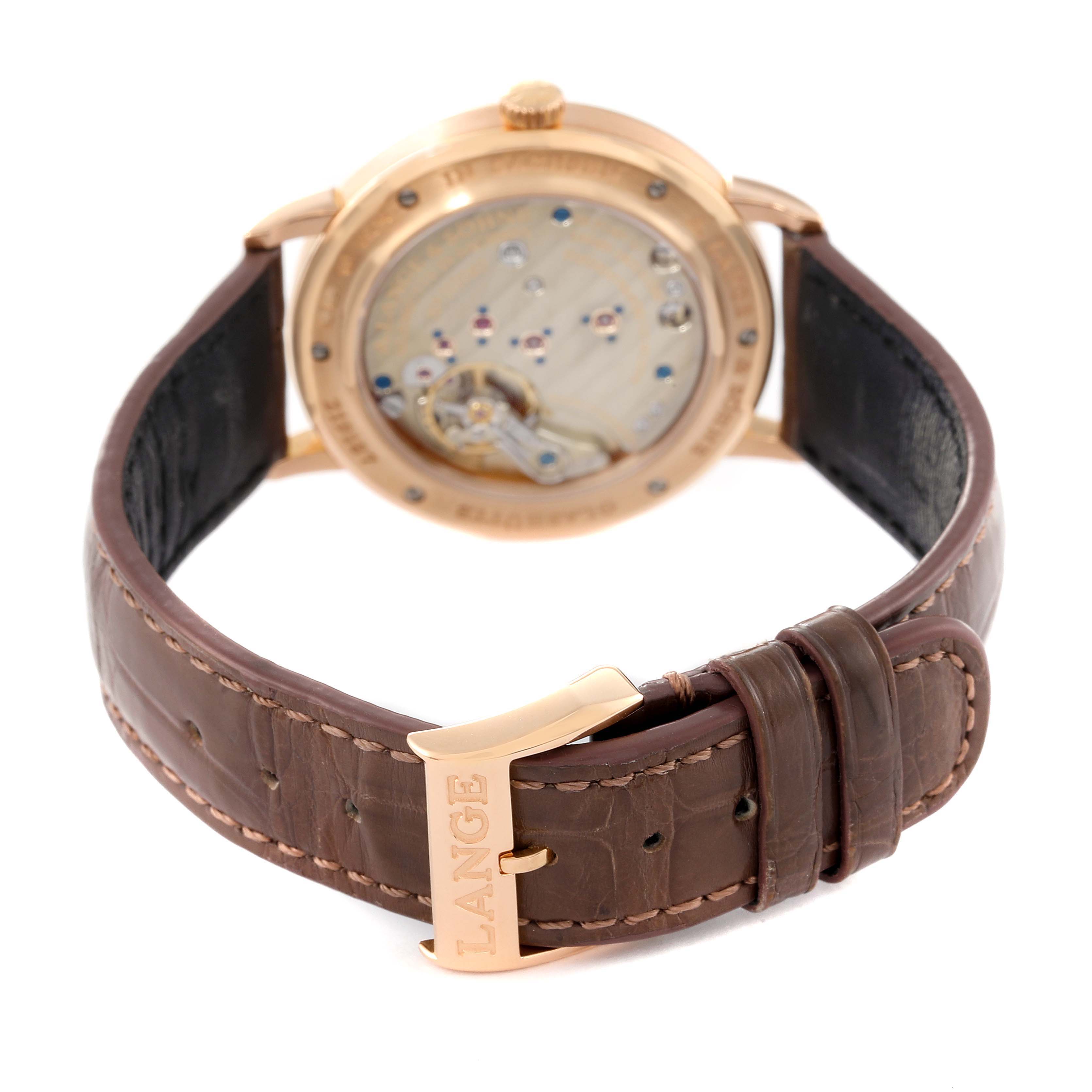 The image shows the back view of an A. Lange & Sohne Saxonia 219.032 Men's Rose Gold Silver Dial watch, displaying its exposed movement and a brown leather strap with "Lange" engraved on the buckle.