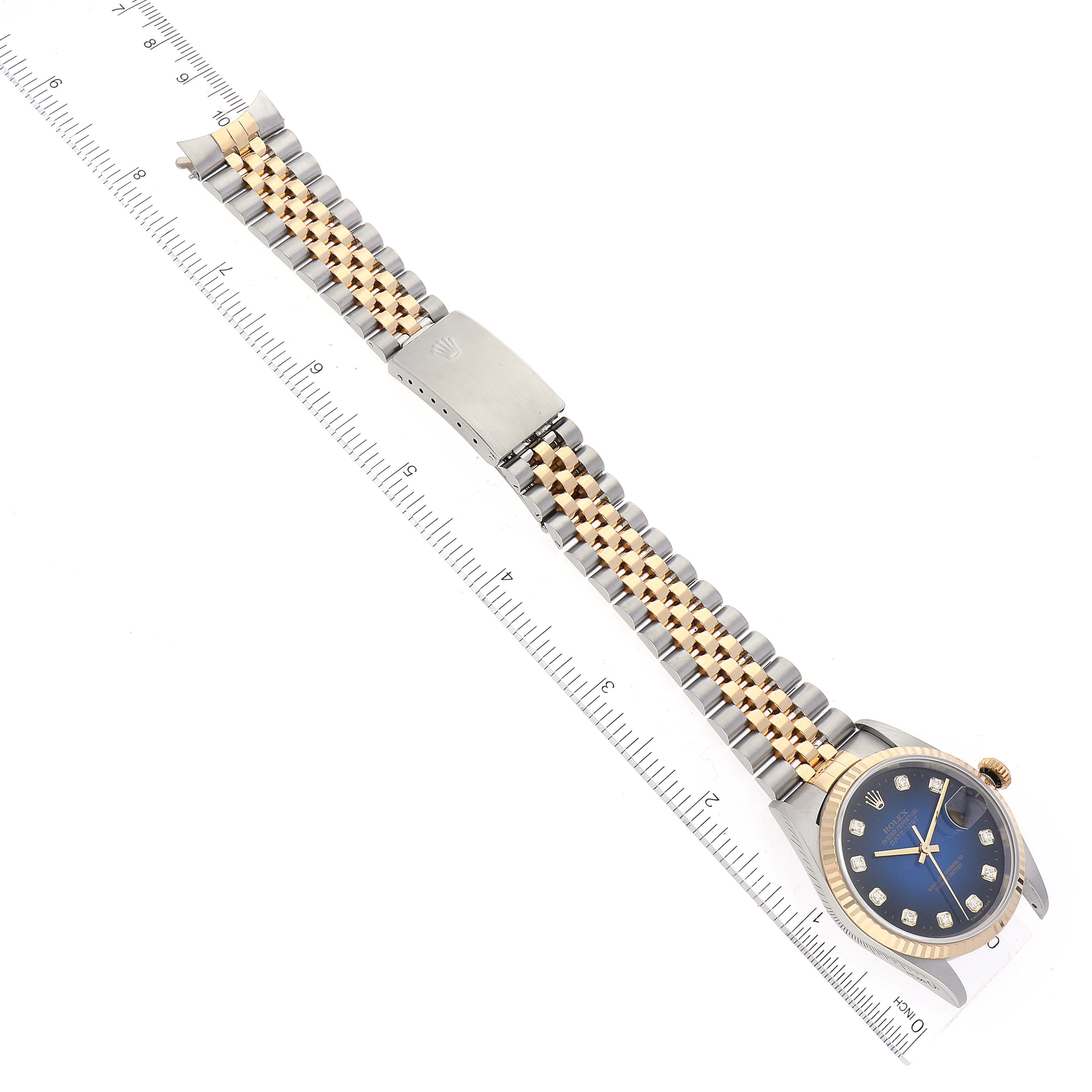 The image shows a Rolex Datejust 16233 Men's Steel and Gold (two tone) Blue Dial 16233 Men's Steel and Gold (two tone) Blue Dial watch in a flat, extended position, featuring its bracelet, dial, and clasp, alongside a ruler.