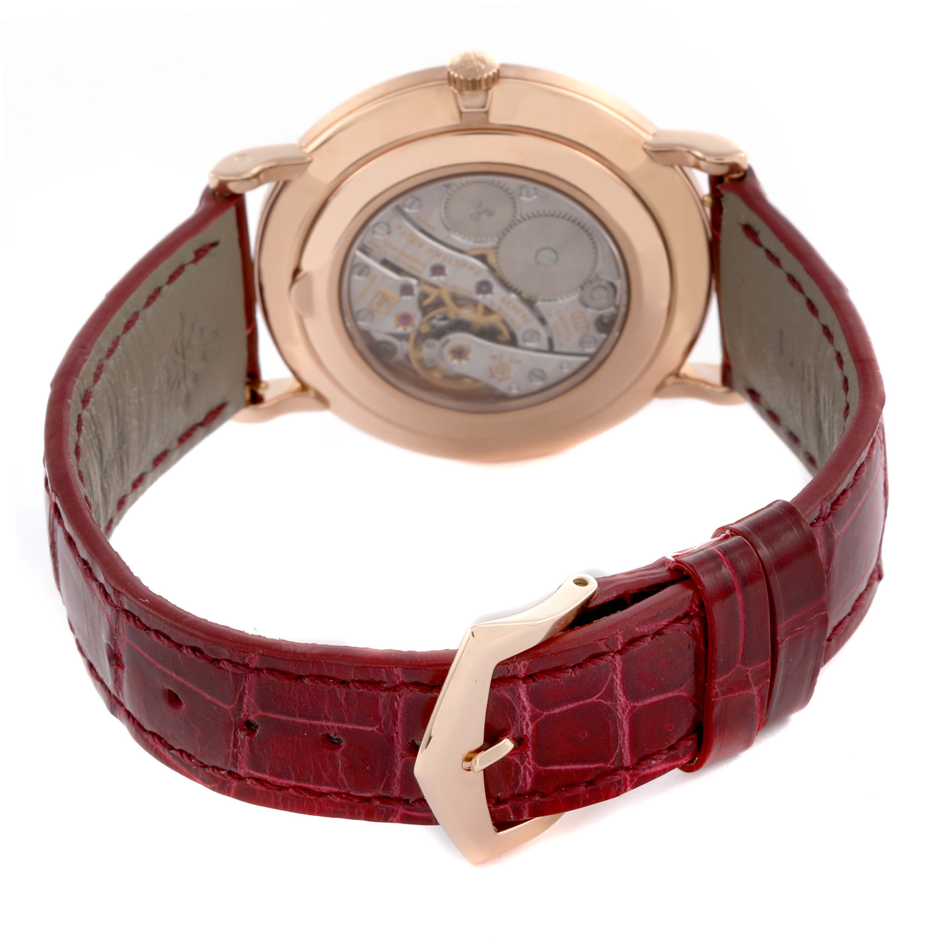 The watch is a Patek Philippe Calatrava 5119R-001 Men's Rose Gold White Dial 5119R-001 Men's Rose Gold White Dial, shown from the back, displaying the movement and a red leather strap with a buckle.