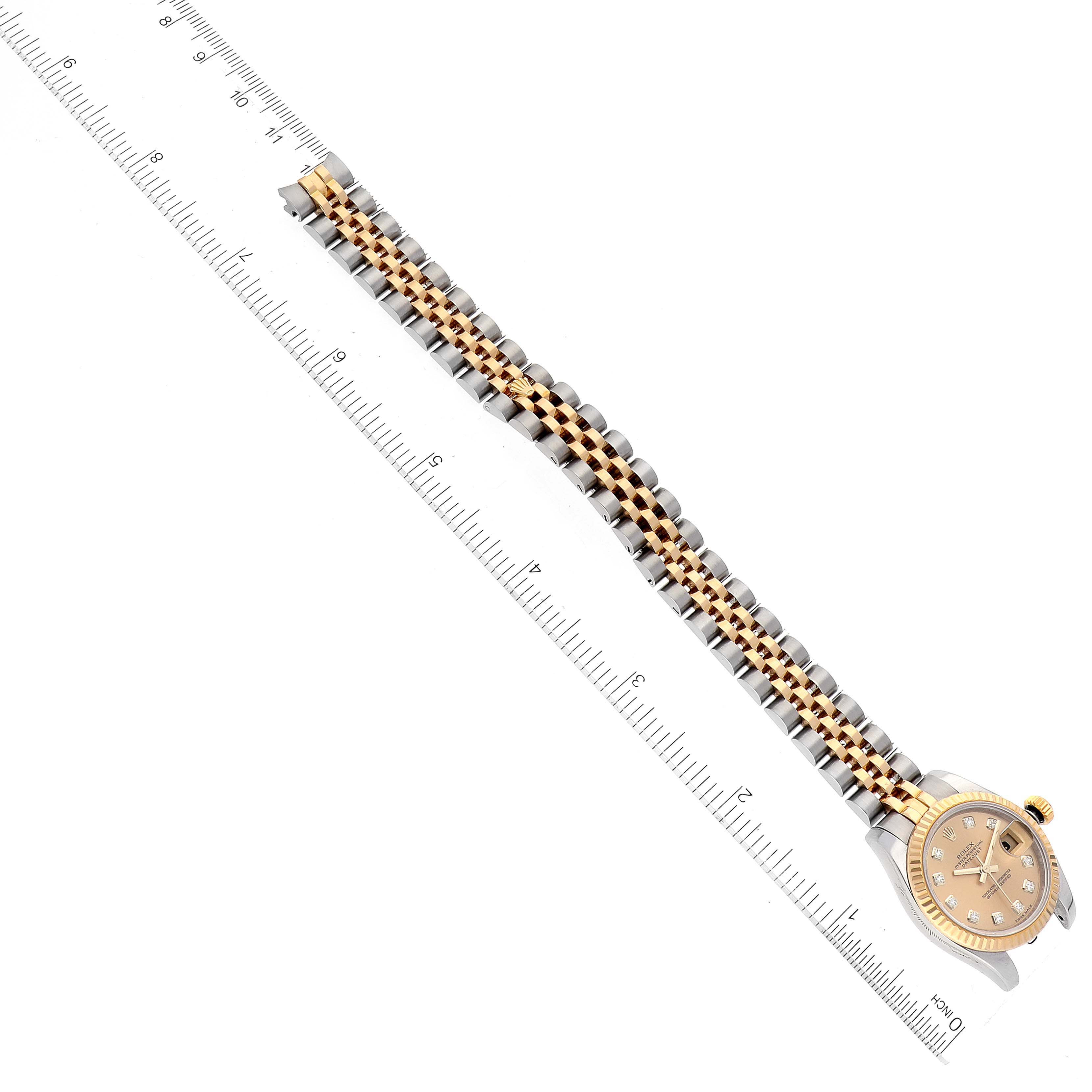 The Rolex Datejust 179173 Women's Steel and Gold (two tone) Champagne Dial 179173 Women's Steel and Gold (two tone) Champagne Dial watch is shown from a top-down angle, highlighting the dial and two-tone bracelet alongside a ruler for measurement.