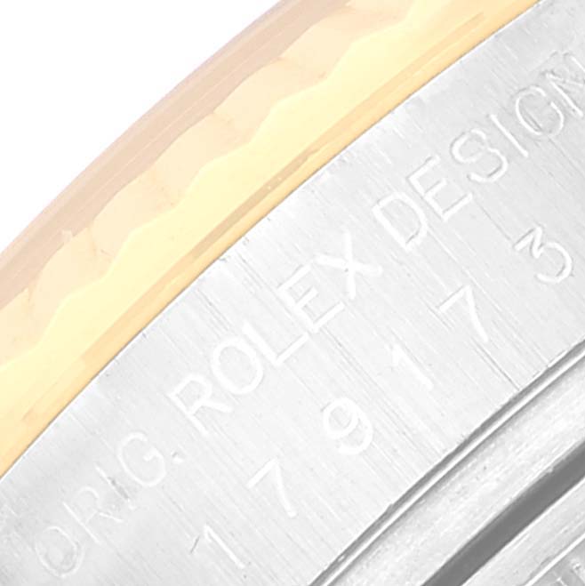 This is a close-up view of the casing on a Rolex Datejust 179173 Women's Steel and Gold (two tone) Silver Dial 179173 Women's Steel and Gold (two tone) Silver Dial watch, showing the engraved "ROLEX DESIGN" text and part of the serial number.
