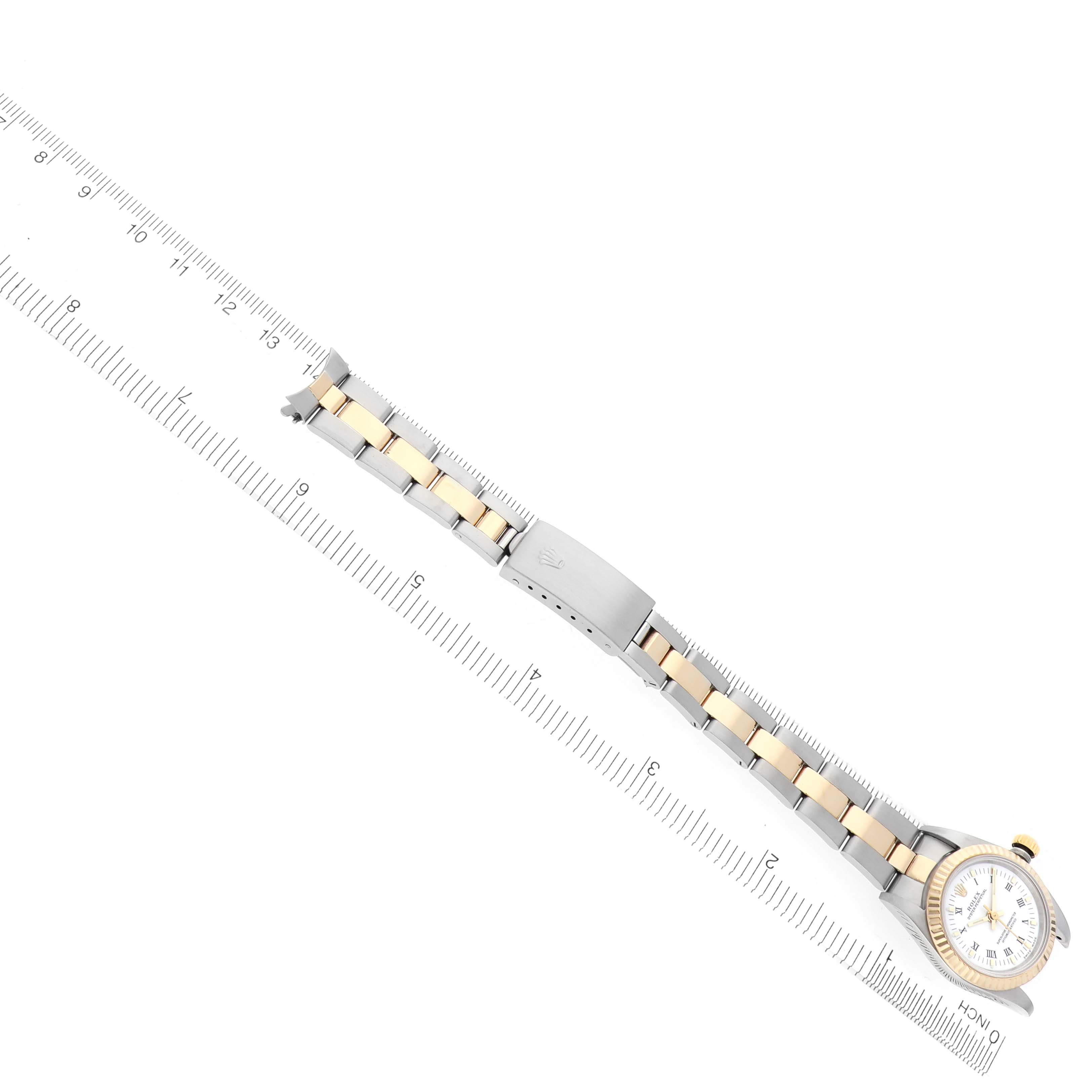 The Rolex Oyster Perpetual 76193 Women
s Steel and Gold (two tone) White Dial 76193 Women
s Steel and Gold (two tone) White Dial watch is shown from a top-down angle, displaying its bracelet, clasp, and watch face alongside a ruler.