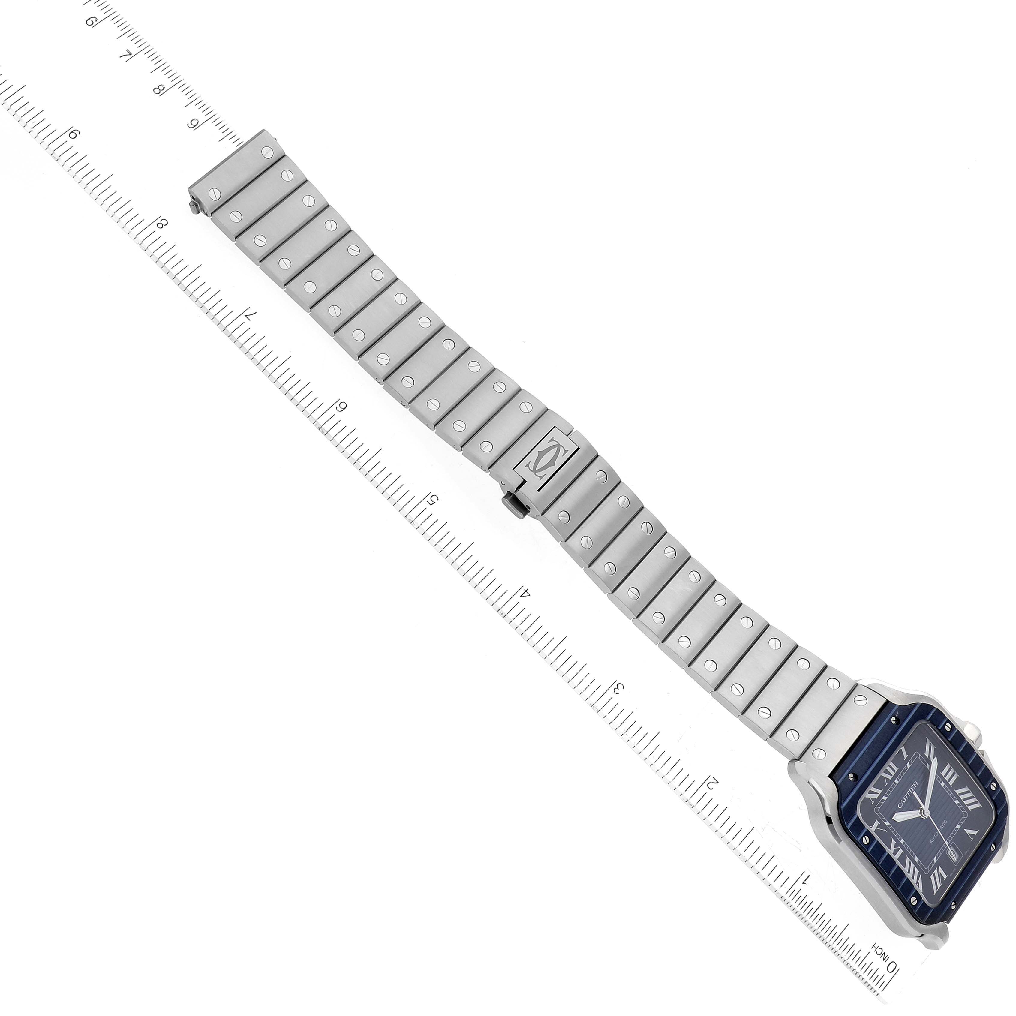 The image shows a Santos de Cartier watch at an angled top-down view, displaying its face and full metal band next to a measuring ruler.