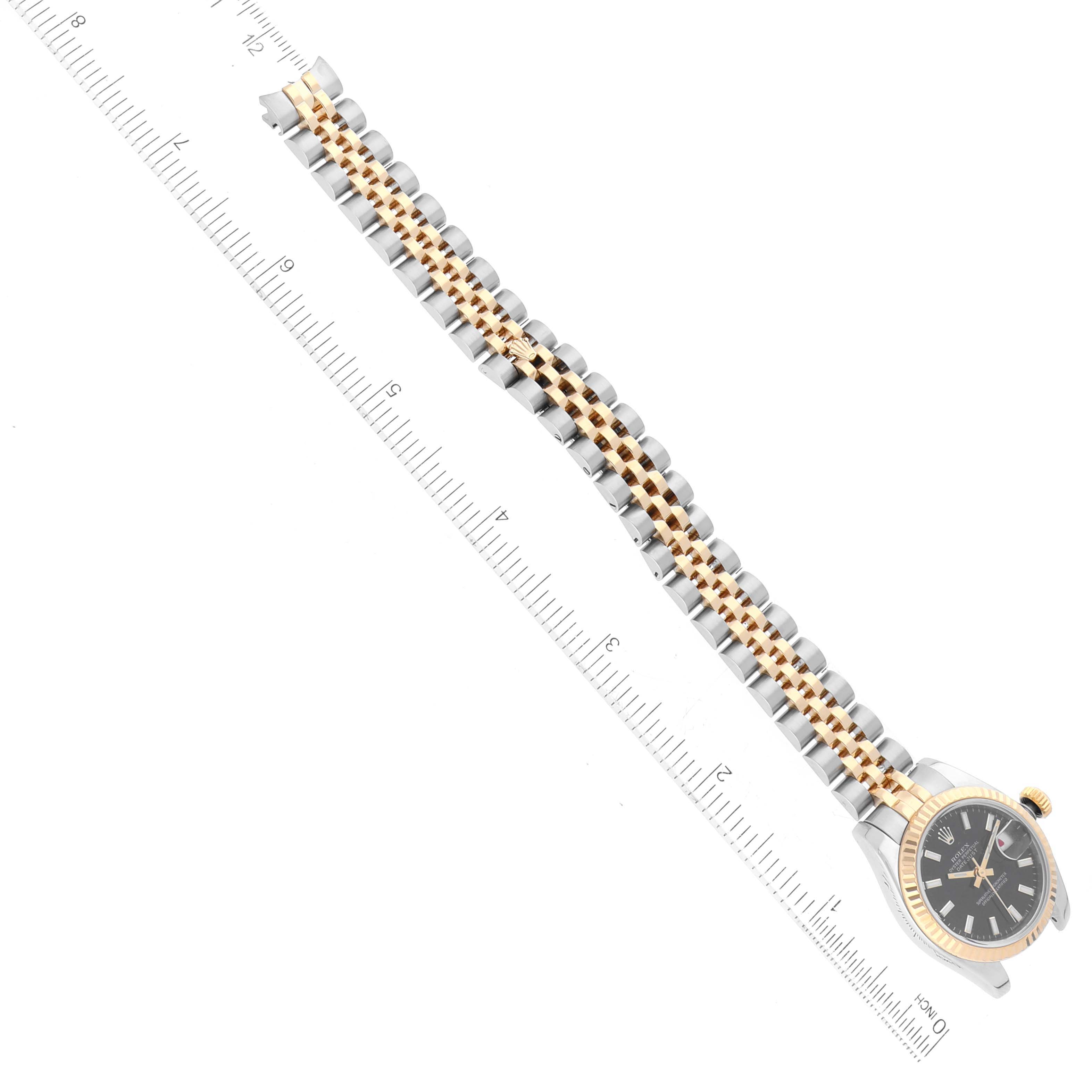 The image shows a Rolex Datejust 179173 Women's Steel and Gold (two tone) Black Dial 179173 Women's Steel and Gold (two tone) Black Dial watch laid flat with the face and entire bracelet visible, alongside a ruler for measurement.