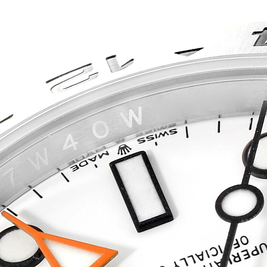 The image shows a close-up of the dial and bezel of a Rolex Explorer 226570 Men
s Stainless Steel White Dial 226570 Men
s Stainless Steel White Dial watch, highlighting the brand logo, markers, and partial hands.